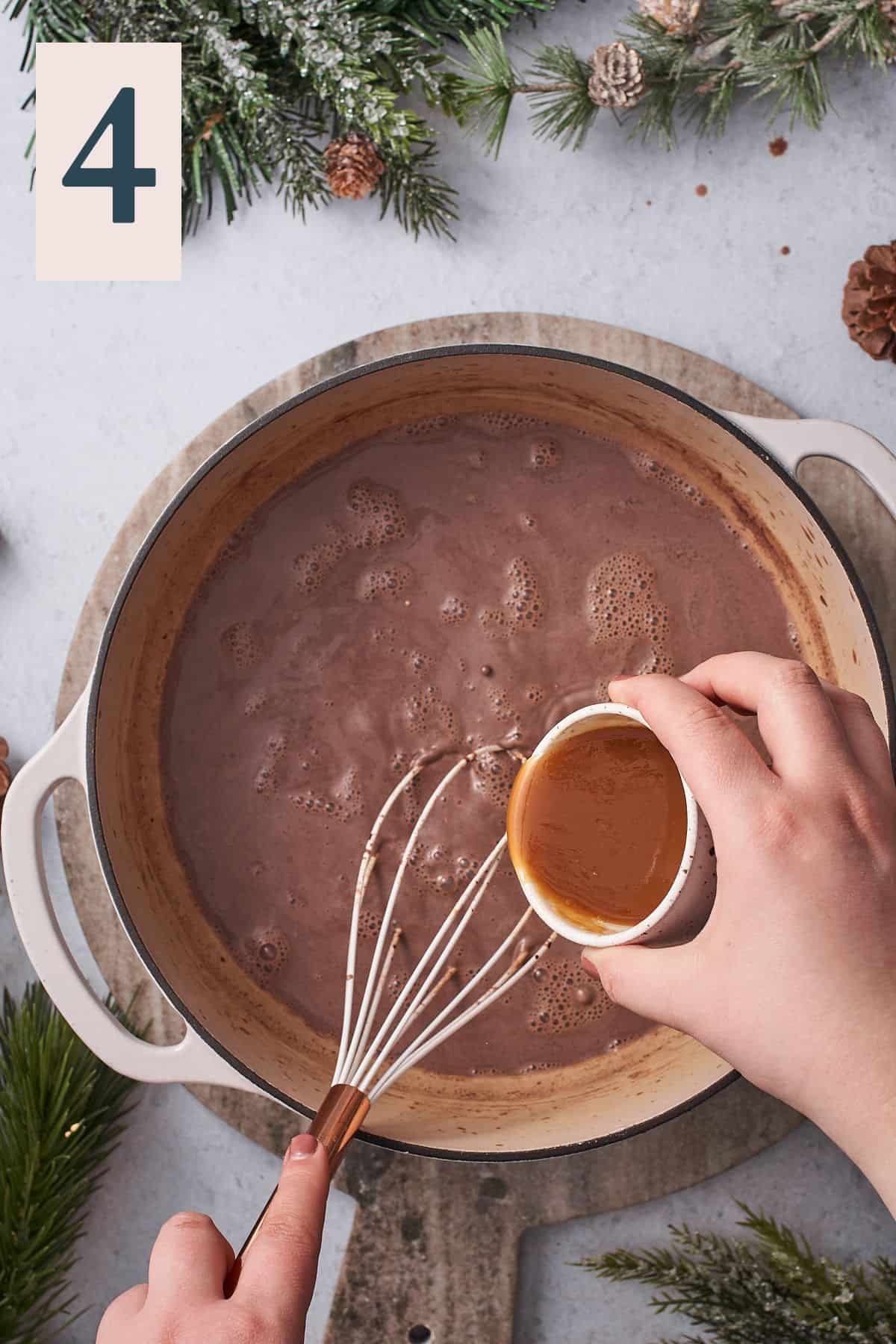 hand pouring salted caramel into a pot of hot chocolate.