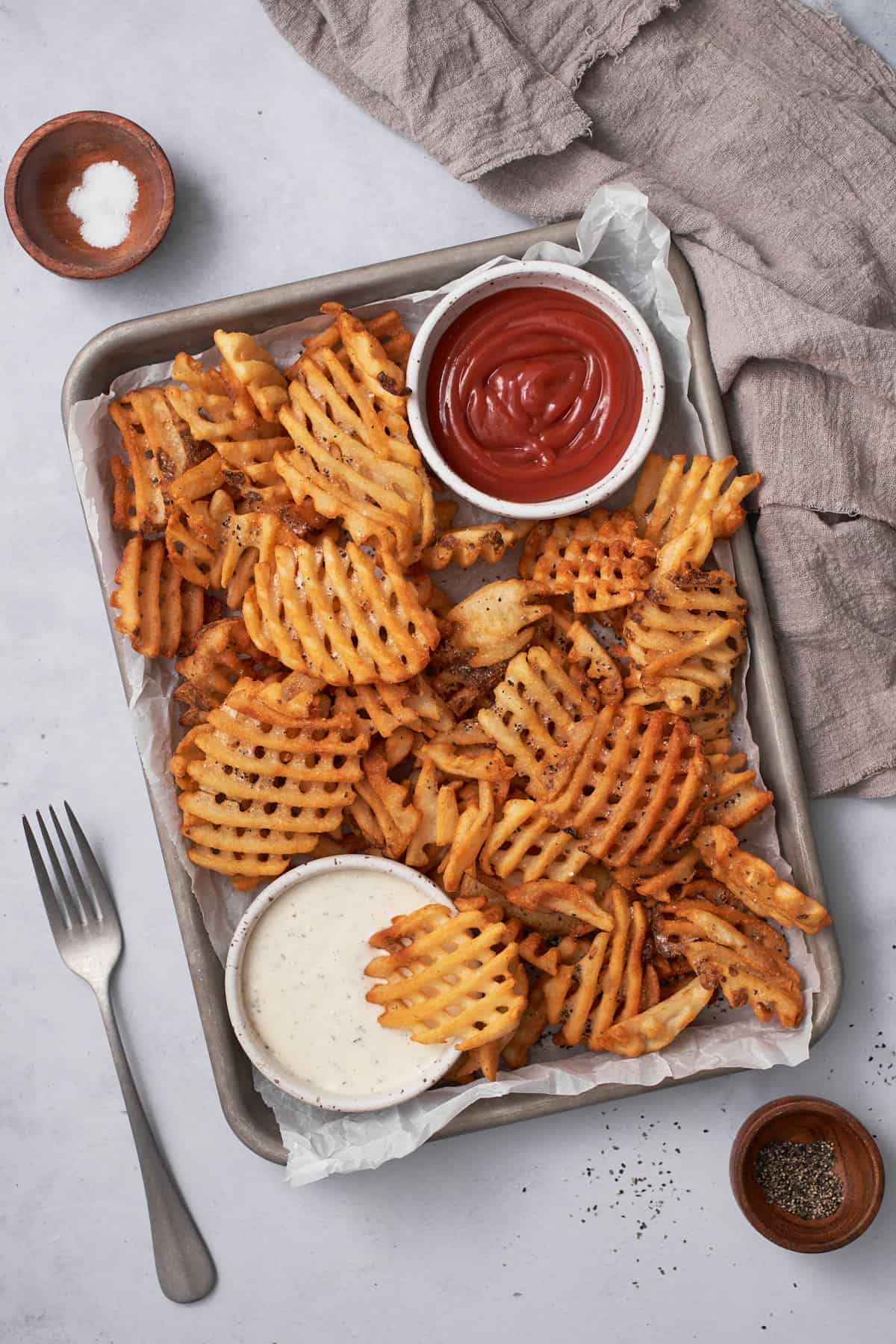Air fryer waffle fries with ketchup and ranch on a baking tray with salt.