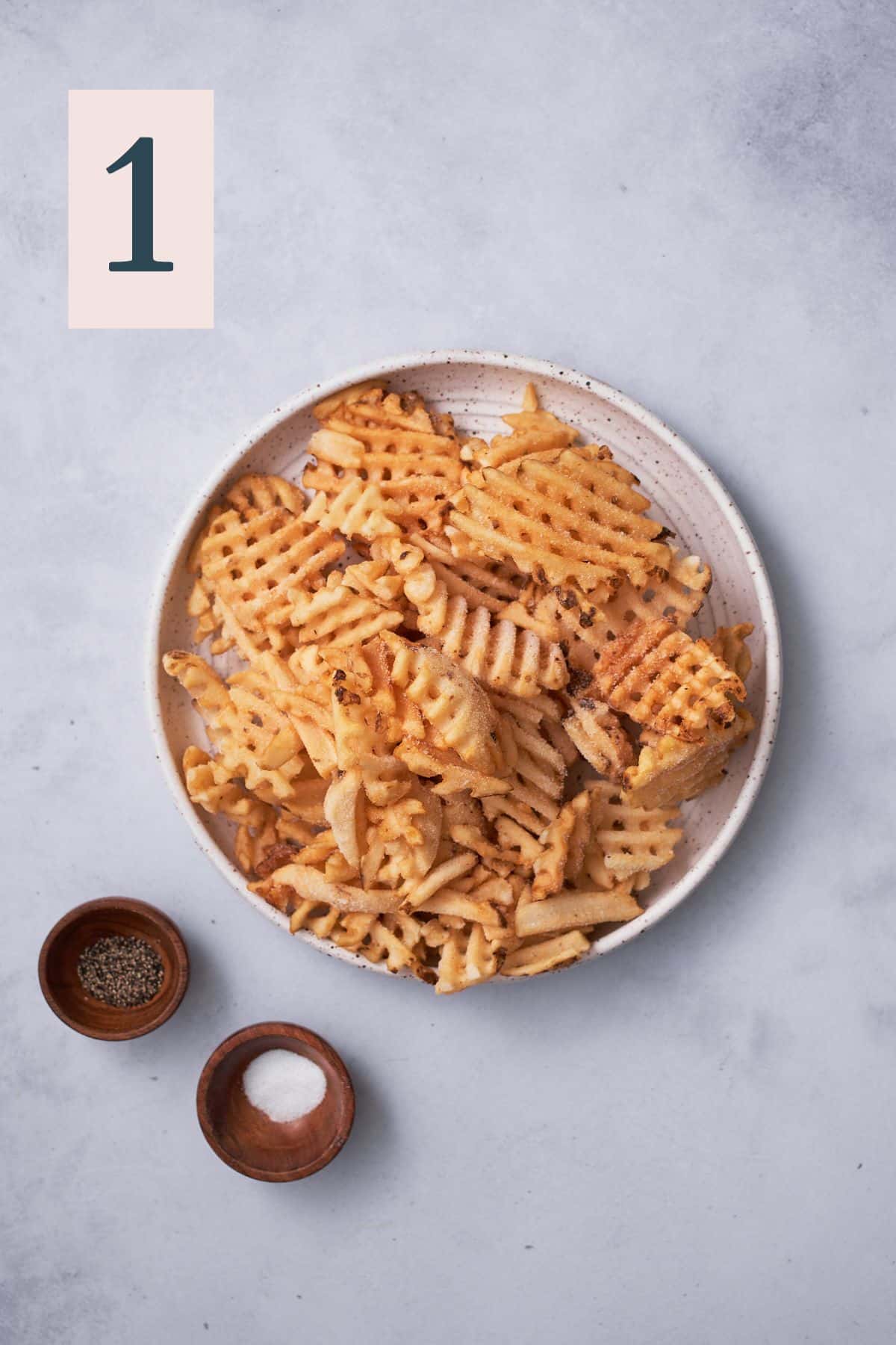 frozen waffle fries on a plate with salt and pepper in round containers.