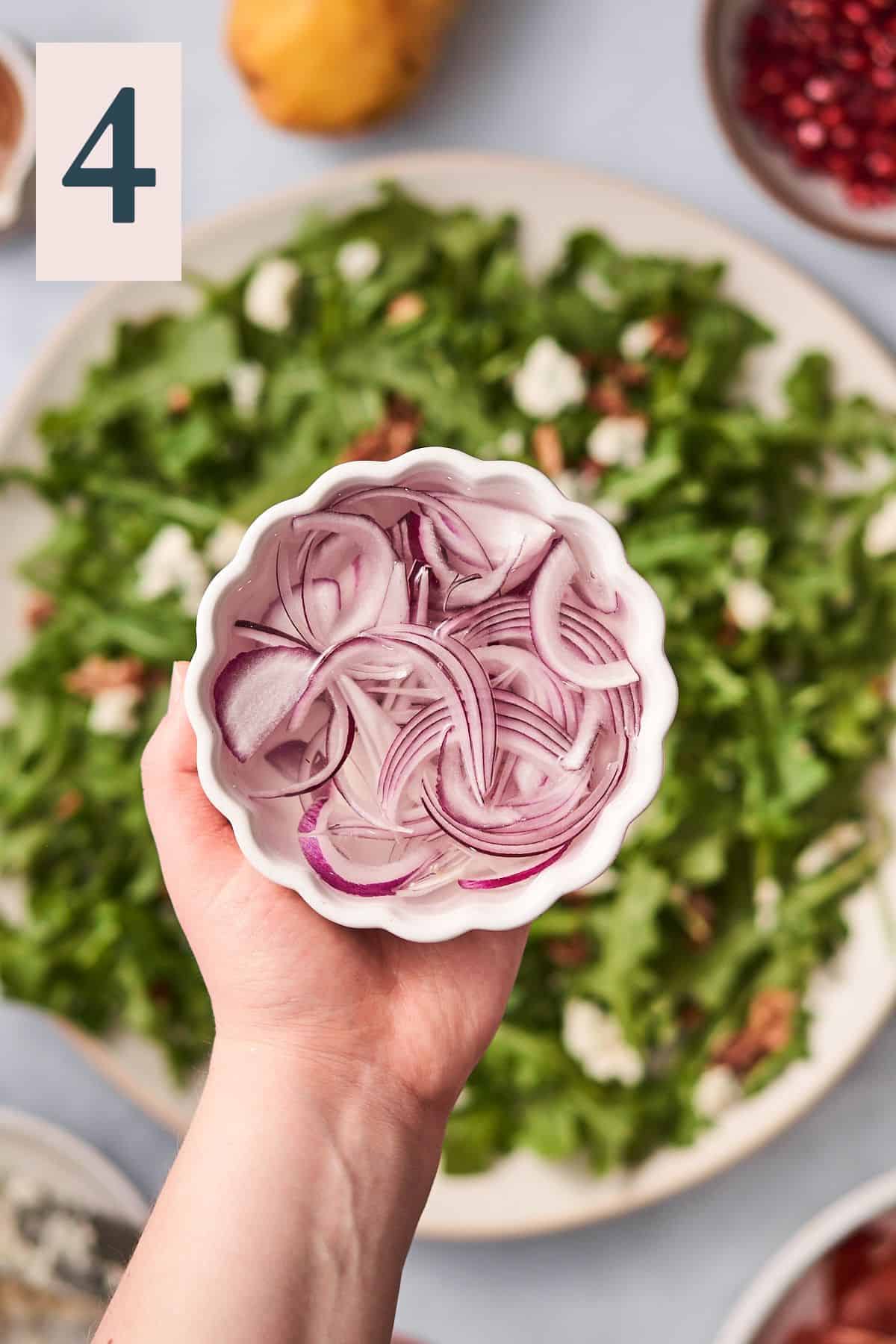 hand holding red onions in water in a small dish overtop of a salad. 