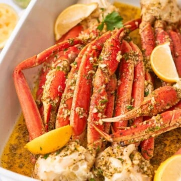 Baked crab legs with lemon wedges and butter pooled at the bottom of the pan.