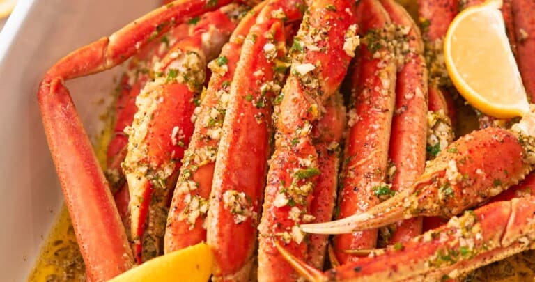 Baked crab legs with lemon wedges and butter pooled at the bottom of the pan.