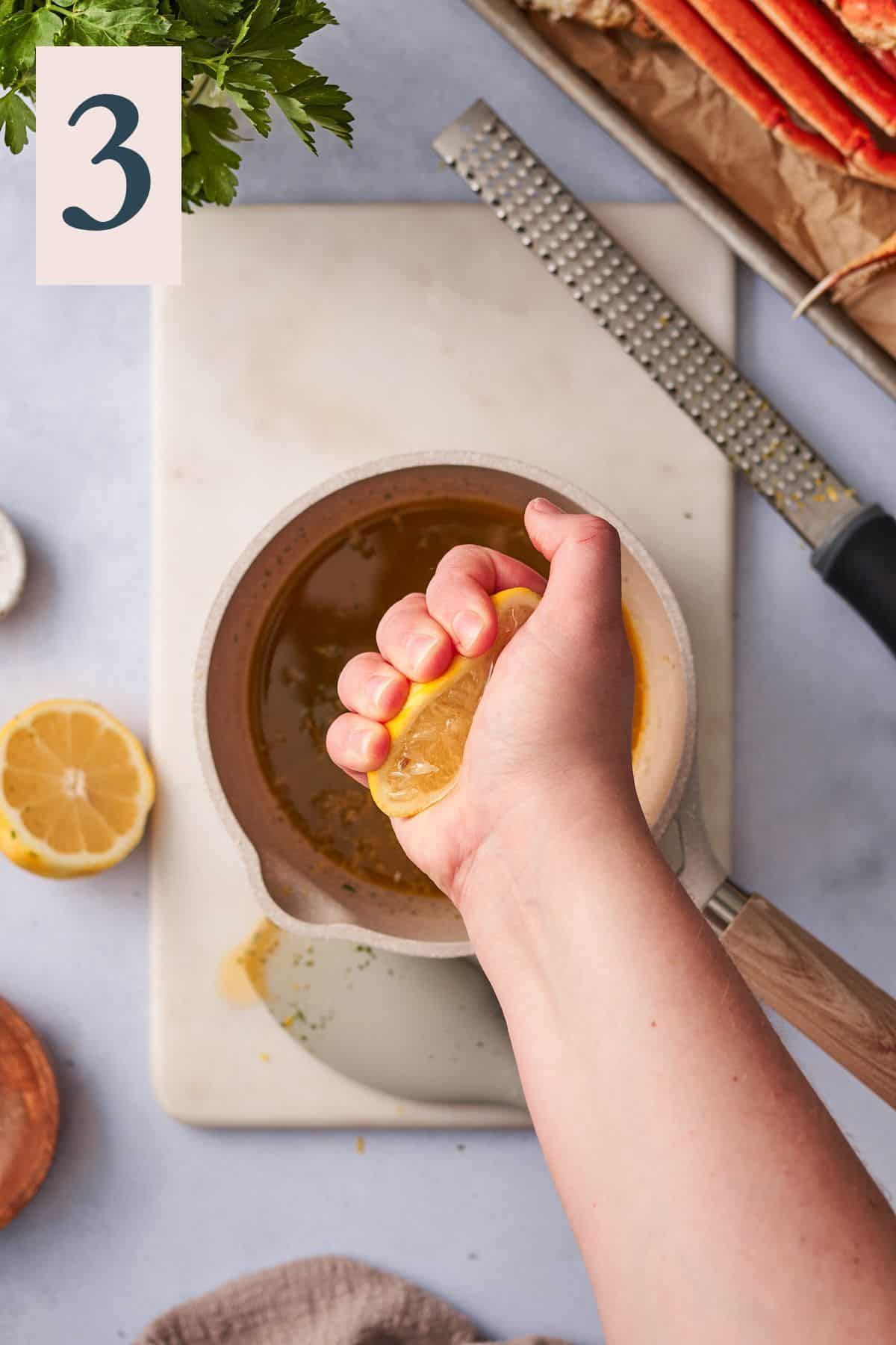 Hand squeezing lemon juice in a sauce pan of garlic butter.