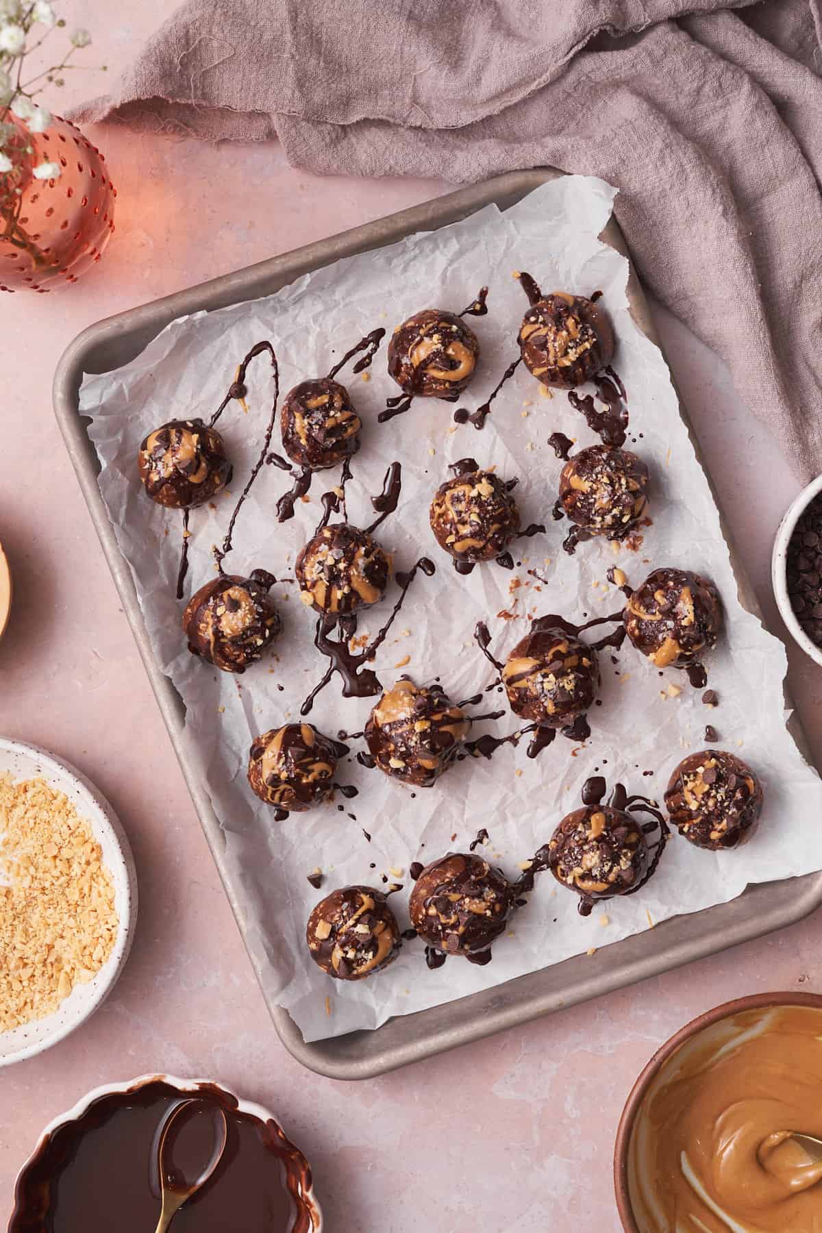 bliss balls on a parchment lined baking sheet drizzled with chocolate, peanut butter, crushed peanuts, chocolate chips, and flaky salt.