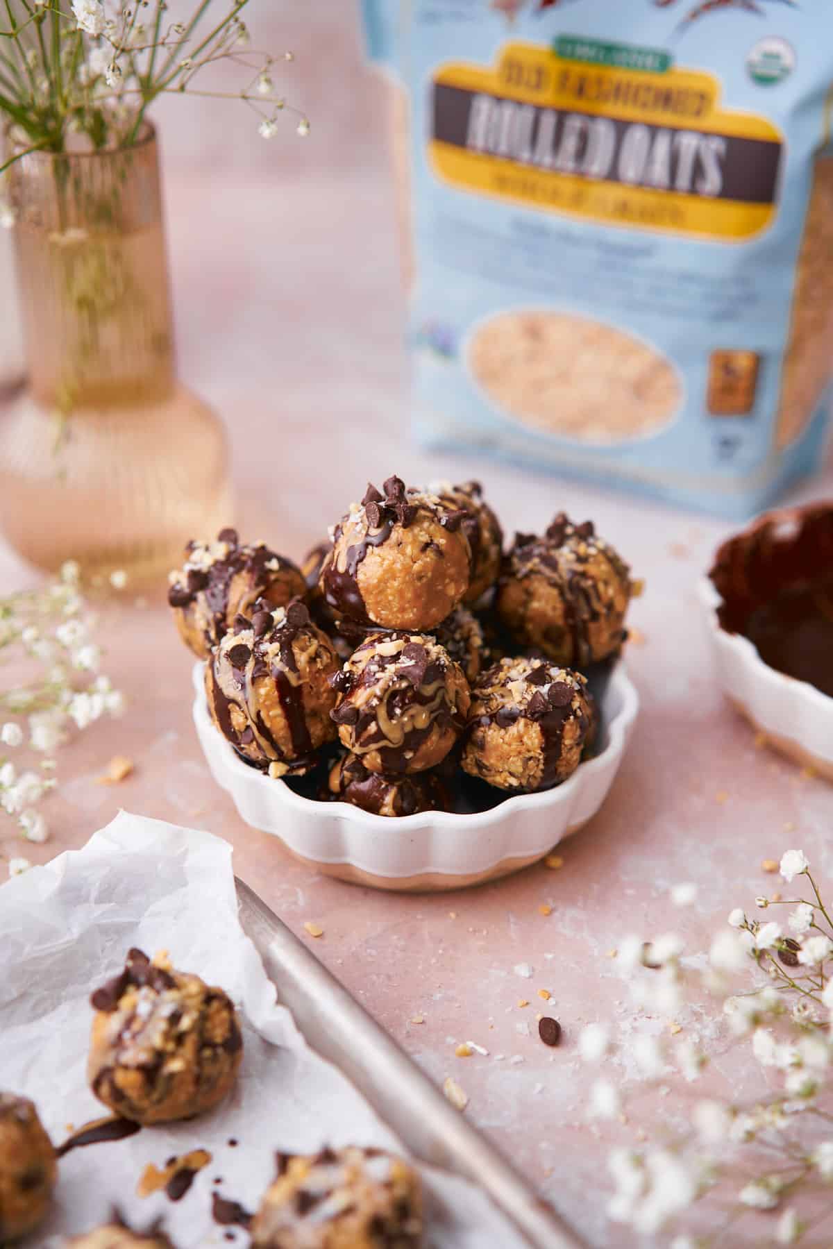Chocolate and peanut butter bliss balls in a dish with flowers and scene surrounding it.