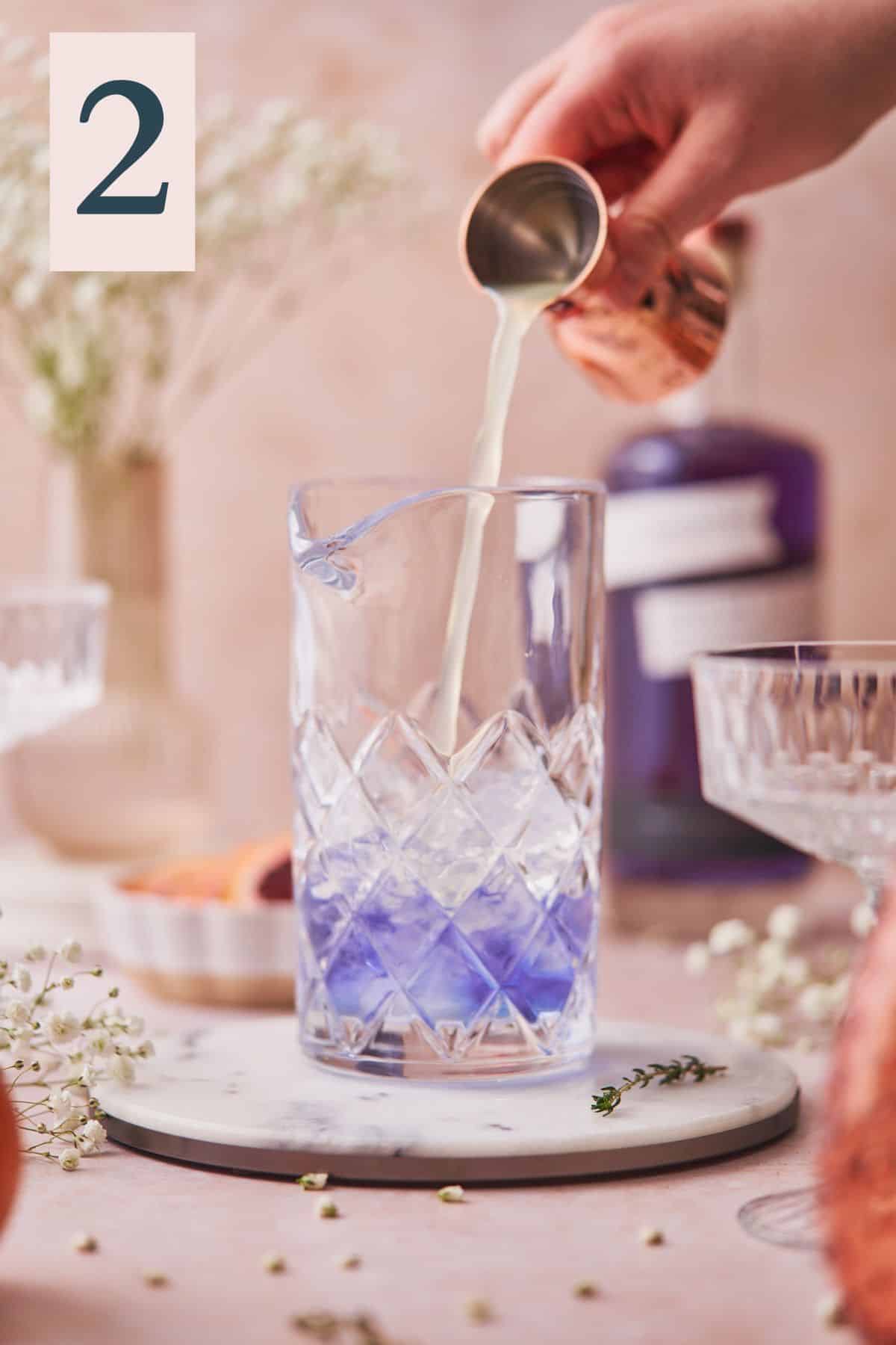 pouring fresh lime juice into a mixing glass with purple gin inside. 