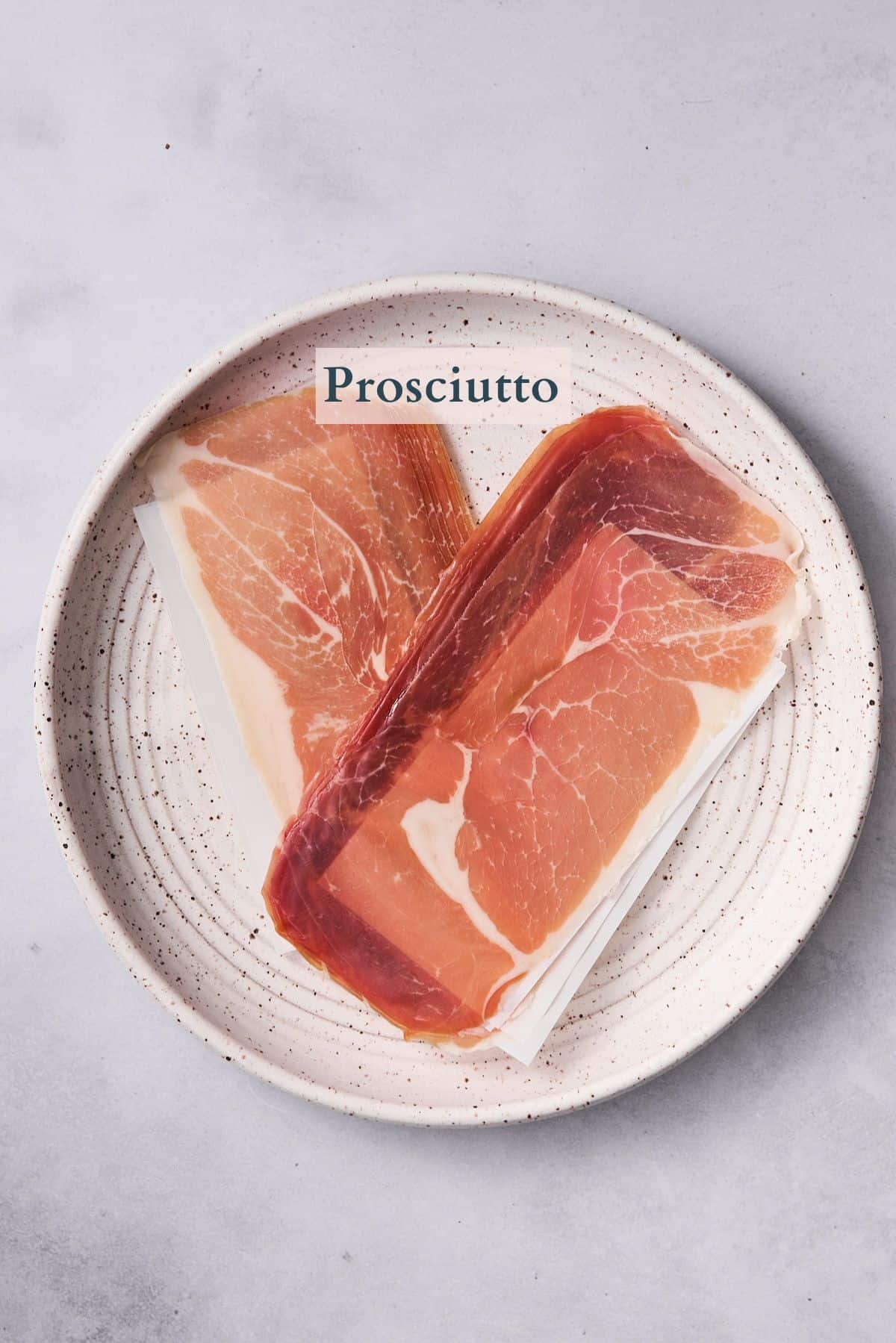 raw prosciutto on a plate with text overlaying to denote that it is prosciutto. 