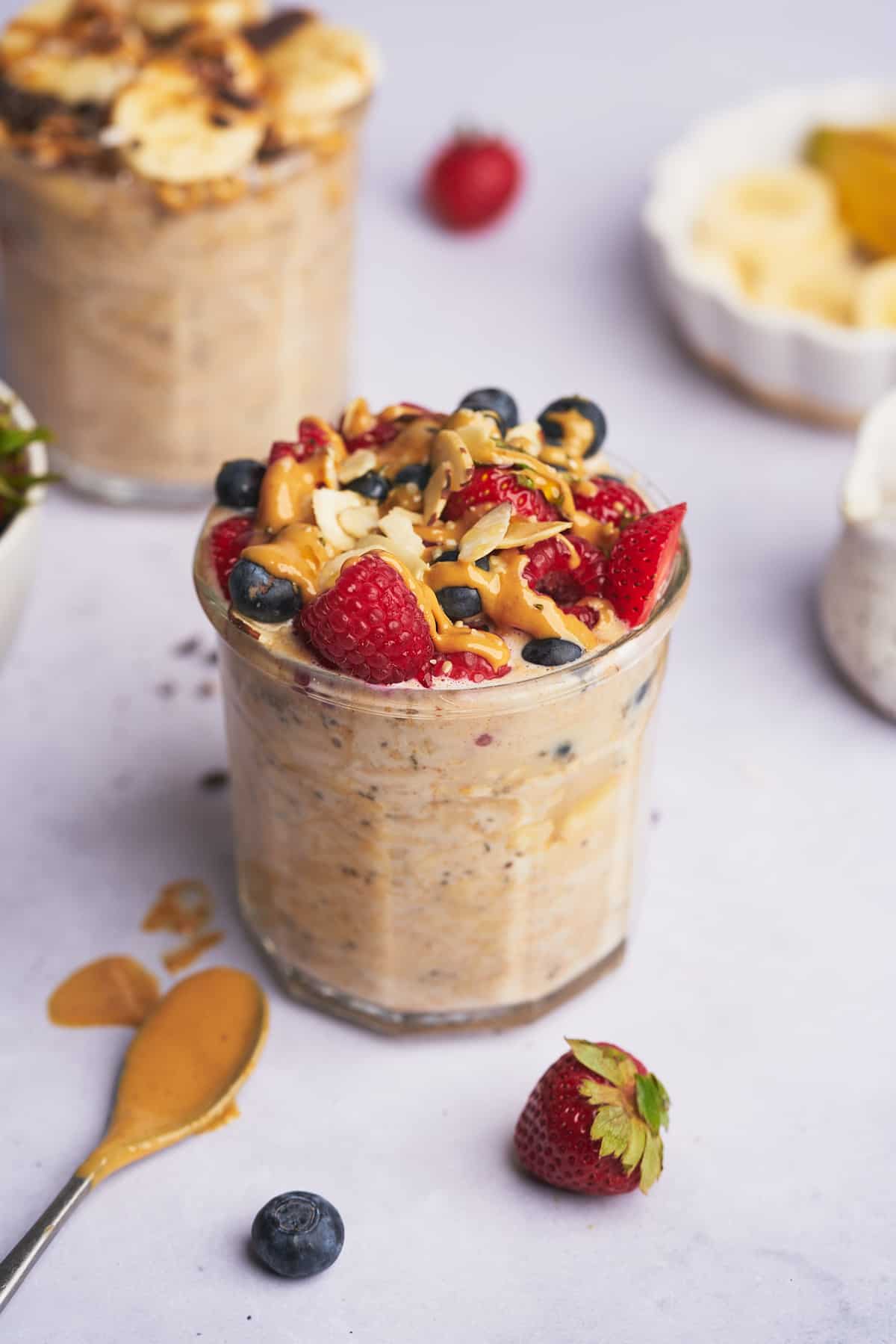 jar of protein overnight oats topped with berries, nuts, and creamy peanut butter with other jars of oats in the background with different toppings.