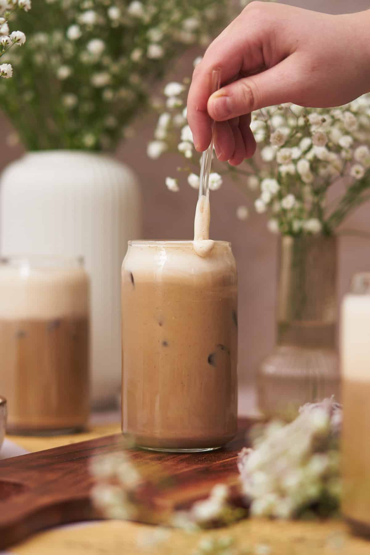 hand stirring protein coffee with a glass straw. 