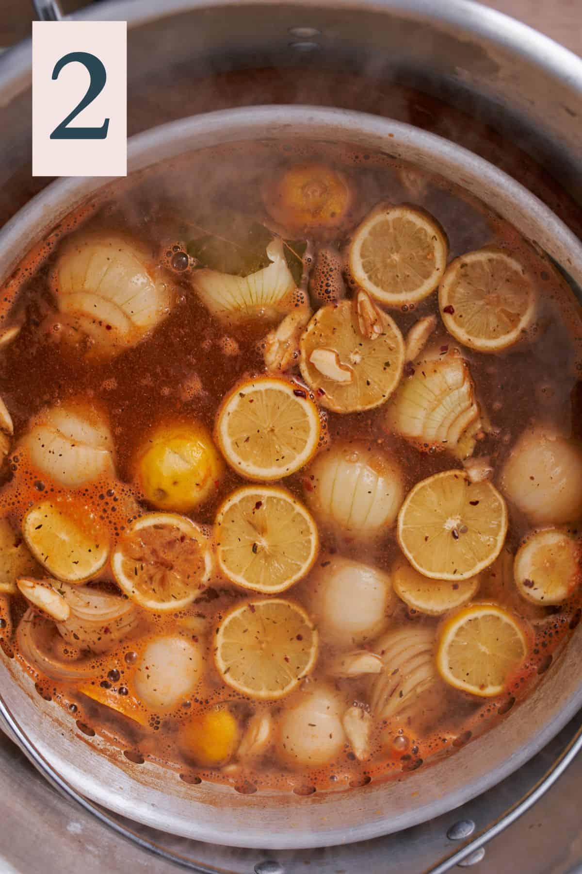 Large stock pot filled with seasoned water with onions, lemon slices, bay leaves, and spicy seasonings.