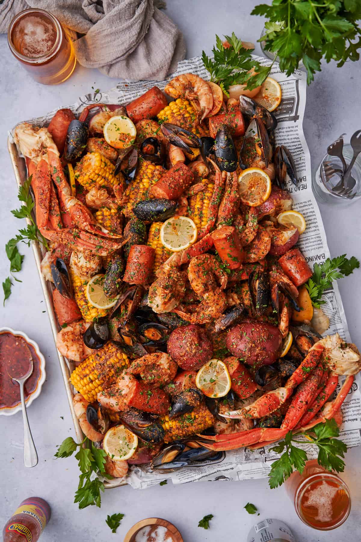 cajun seafood boil on a baking sheet with fresh parsley, lemon, potatoes, butter, and beer. 