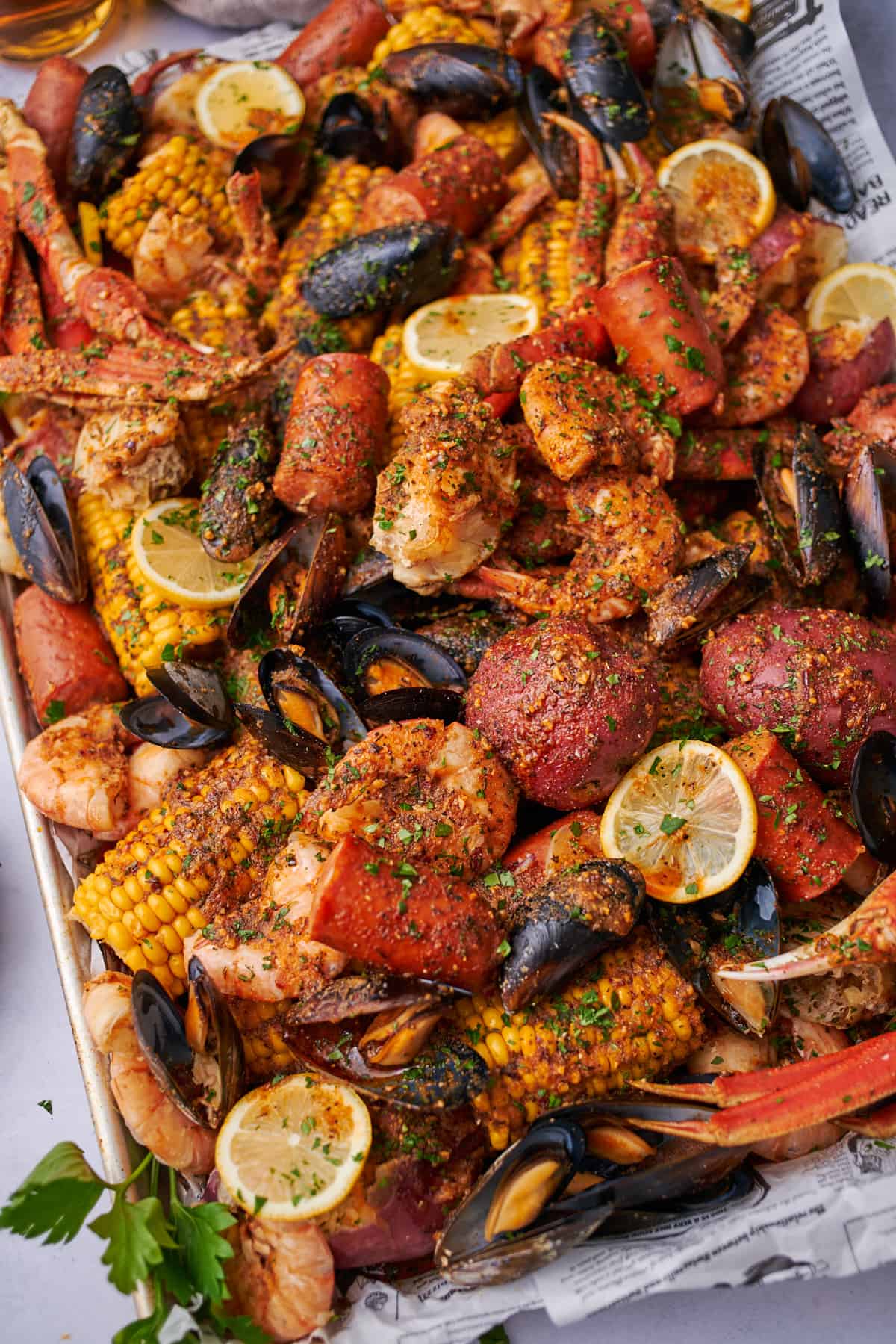 Cajun seafood boil on a baking sheet with newspaper lining, with potatoes, corn, shrimp, sausage, and more.