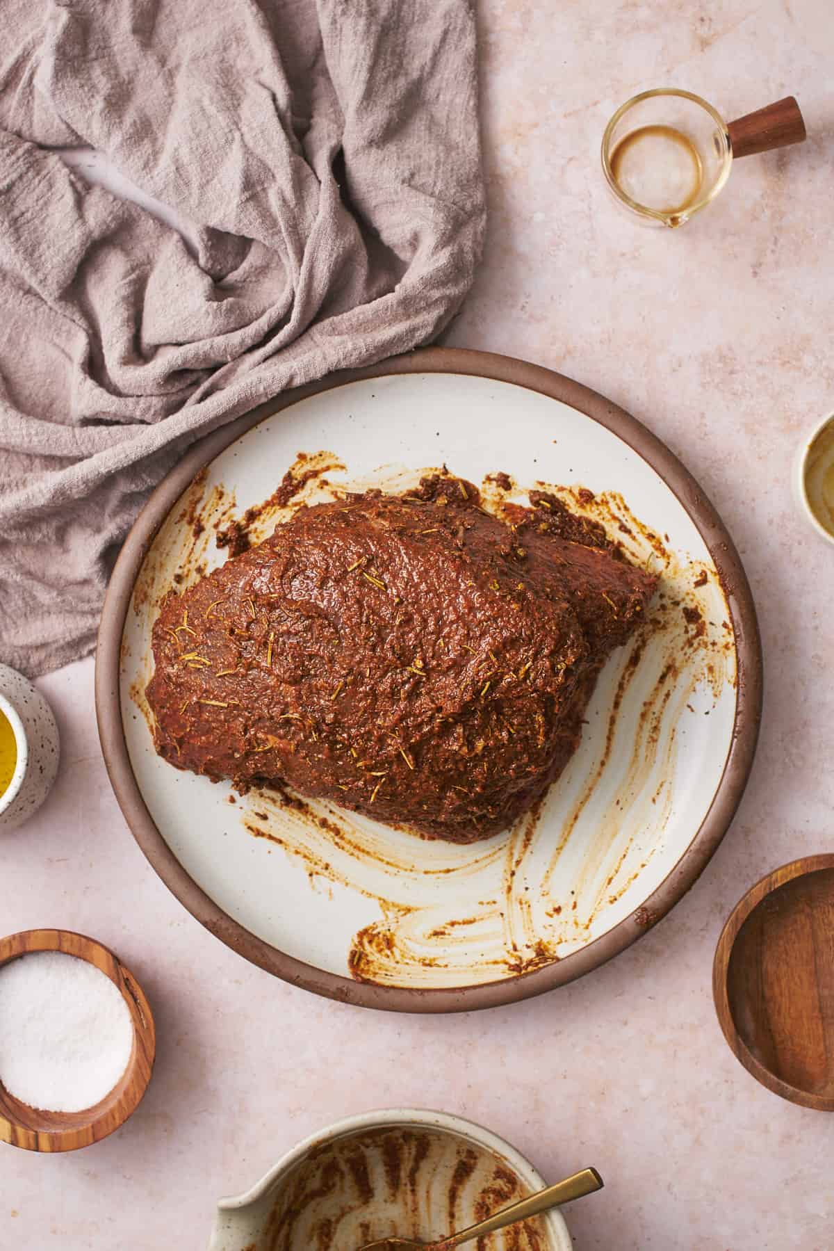 Coating a beef roast in mustard and seasonings on a plate.