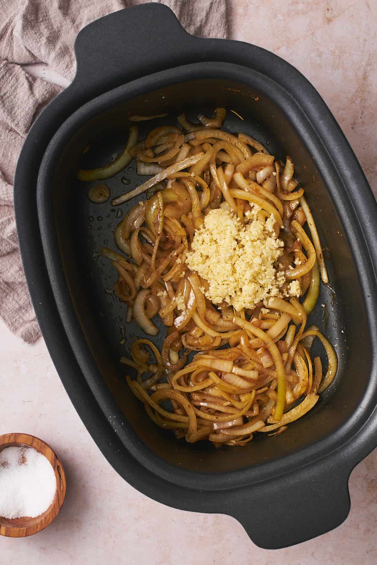 Cooked onions in a slow cooker topped with lots of freshly minced garlic.