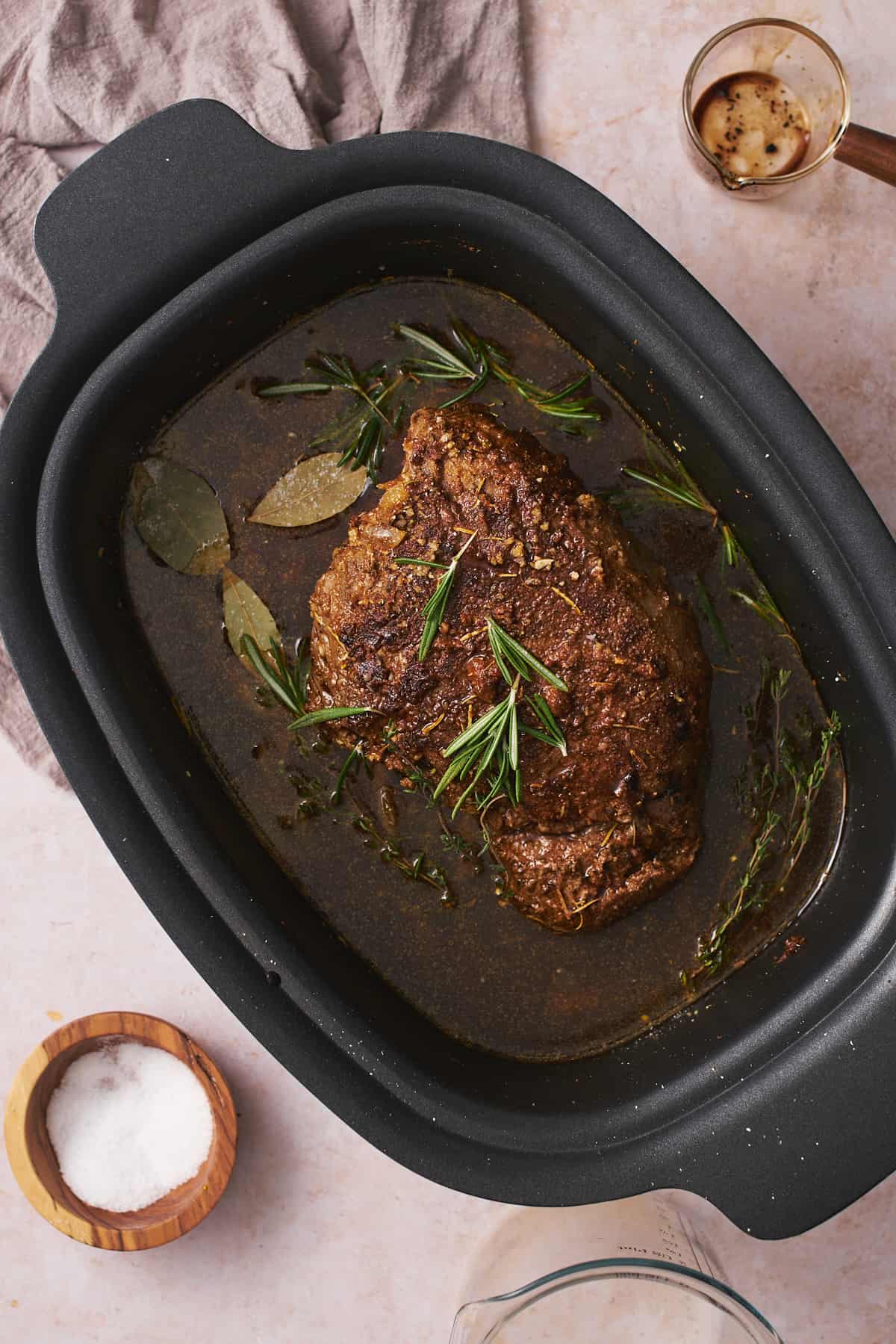 Browned roast in a slow cooker with broth, and herbs.