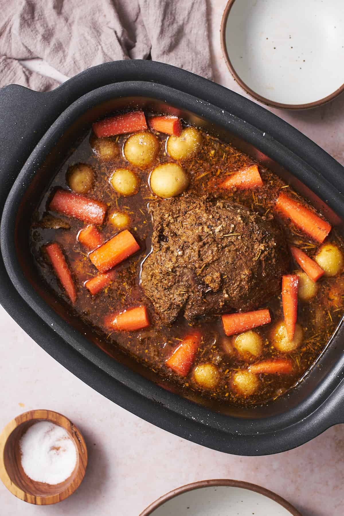 Potatoes and carrots added to a slow cooker with a beef roast.