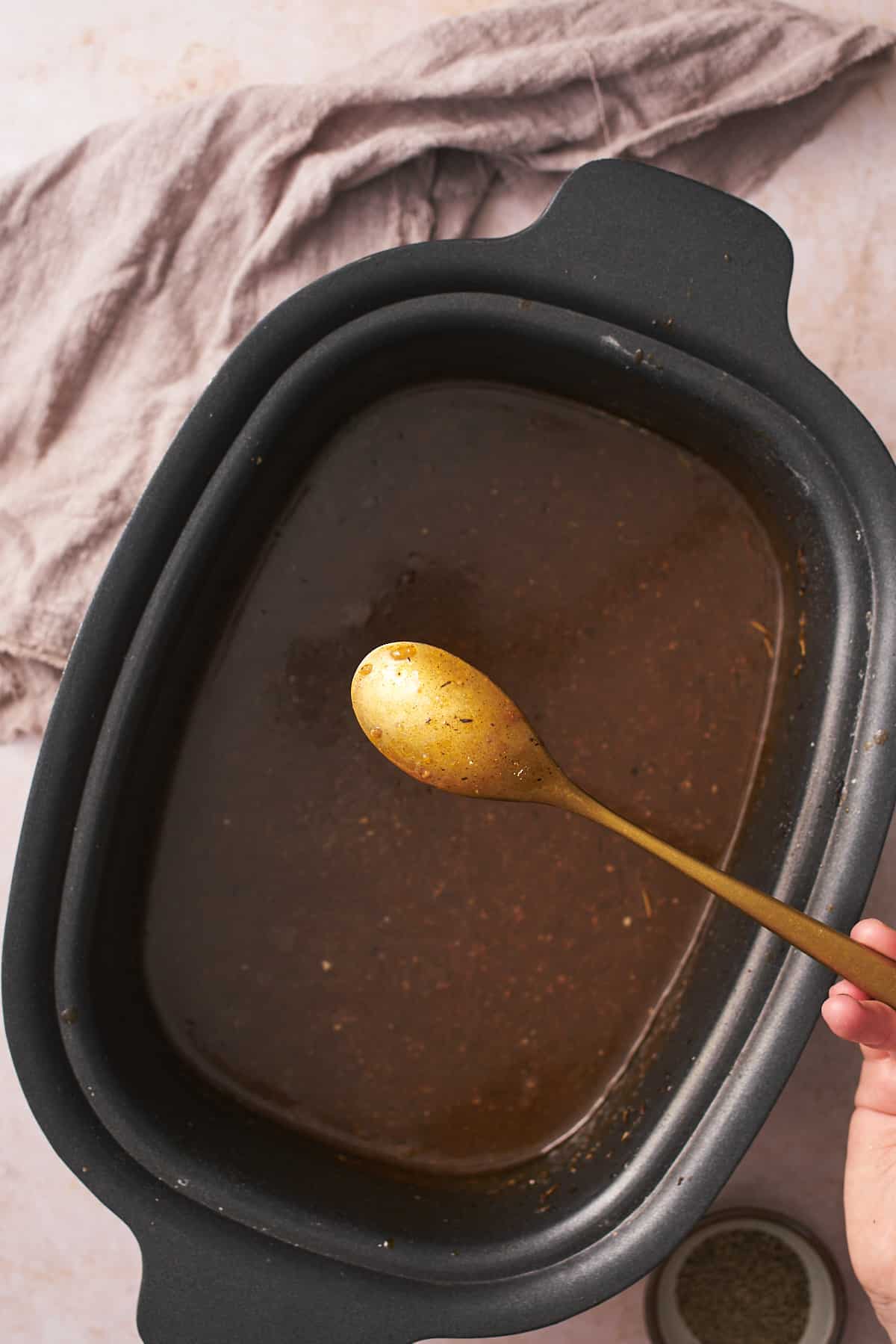 Gravy in a slow cooker with a spoon held up to the camera with gravy coating the back of a spoon.