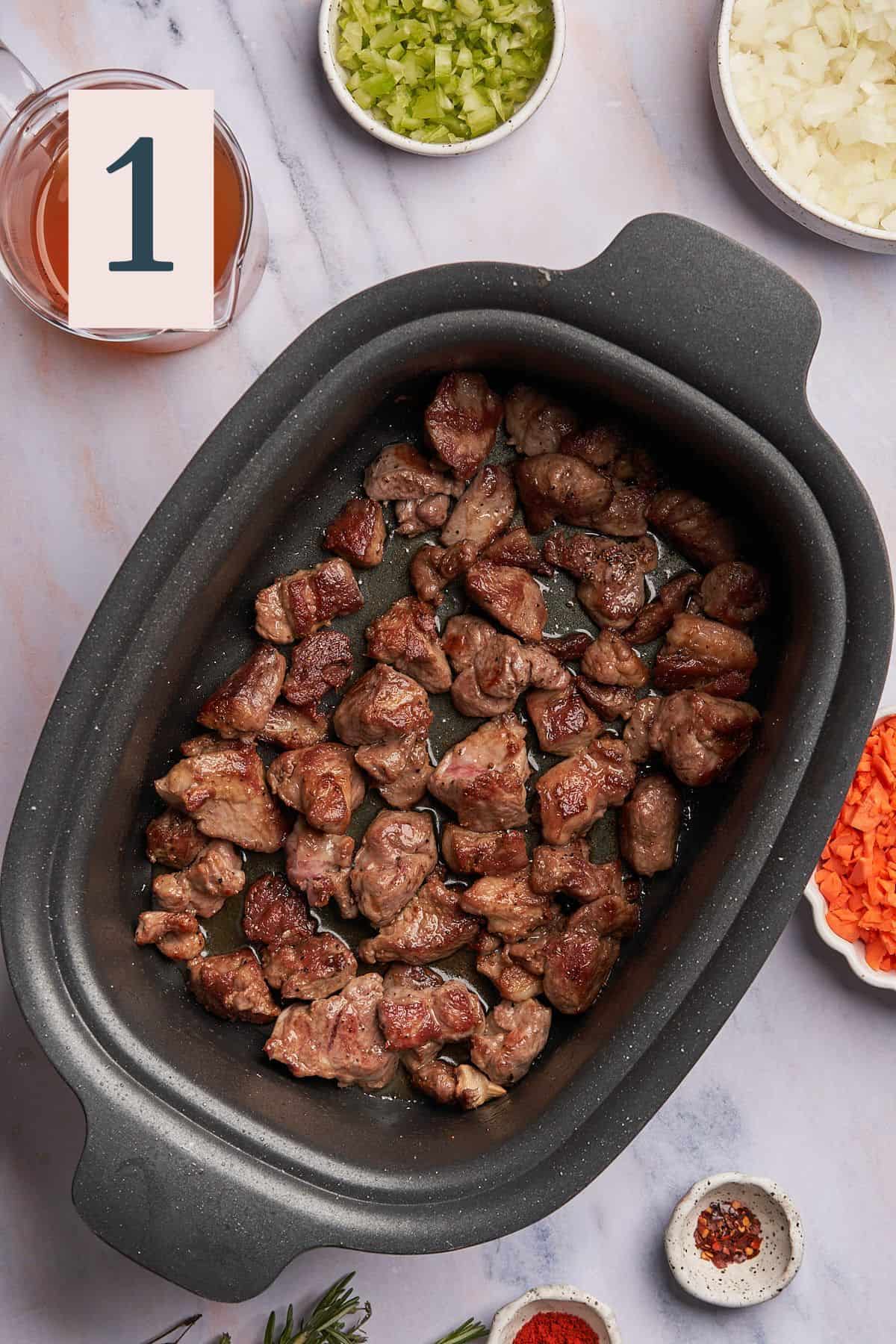 cooked pieces of lamb in a large slow cooker with browned bits.