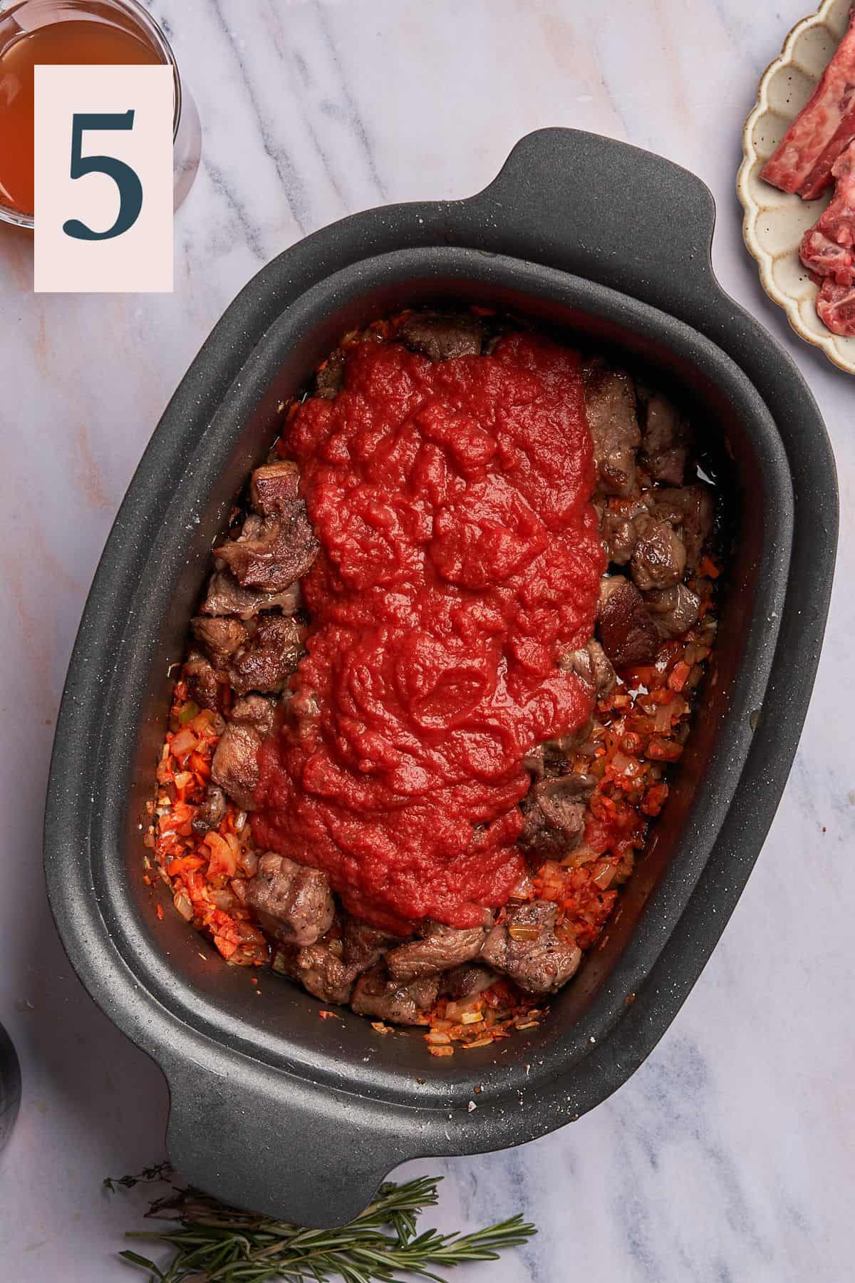 lamb chunks in a slow cooker with crushed tomatoes and cooked vegetables. 
