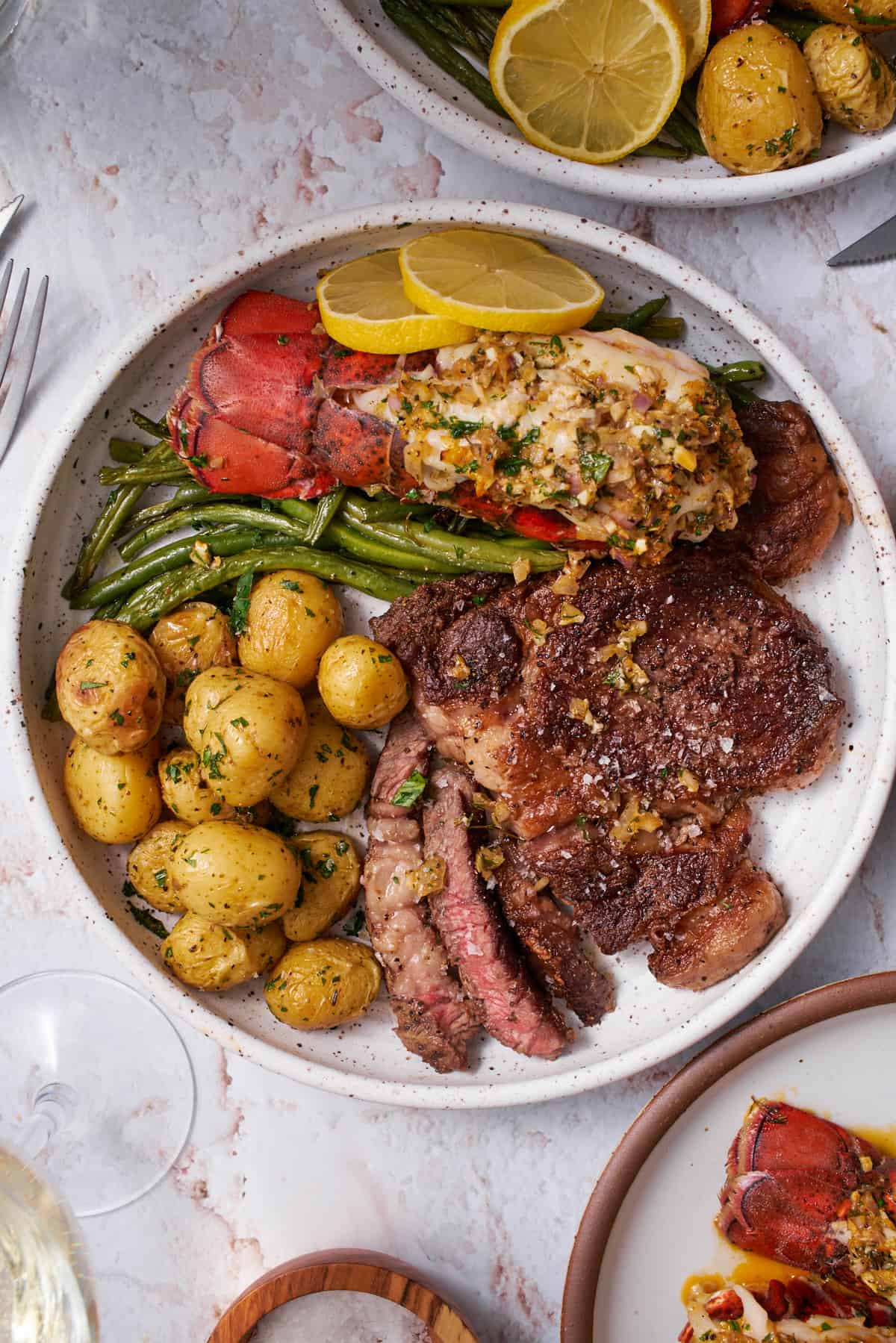 steak and lobster recipe with steak, potatoes, green beans, and lemon on a plate.