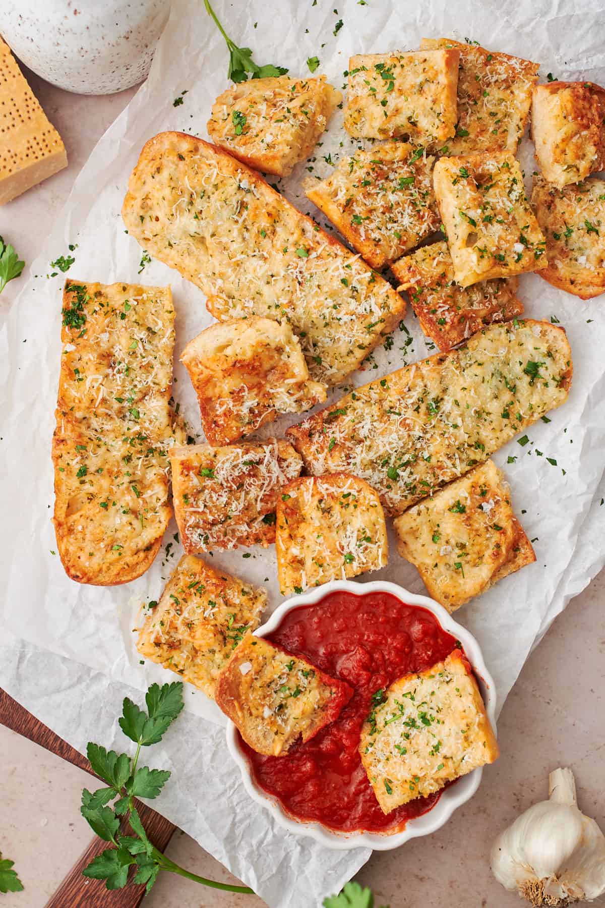 close up shot of air fryer garlic bread on white parchment paper, with some of the pieces in a bowl of marinara sauce. 