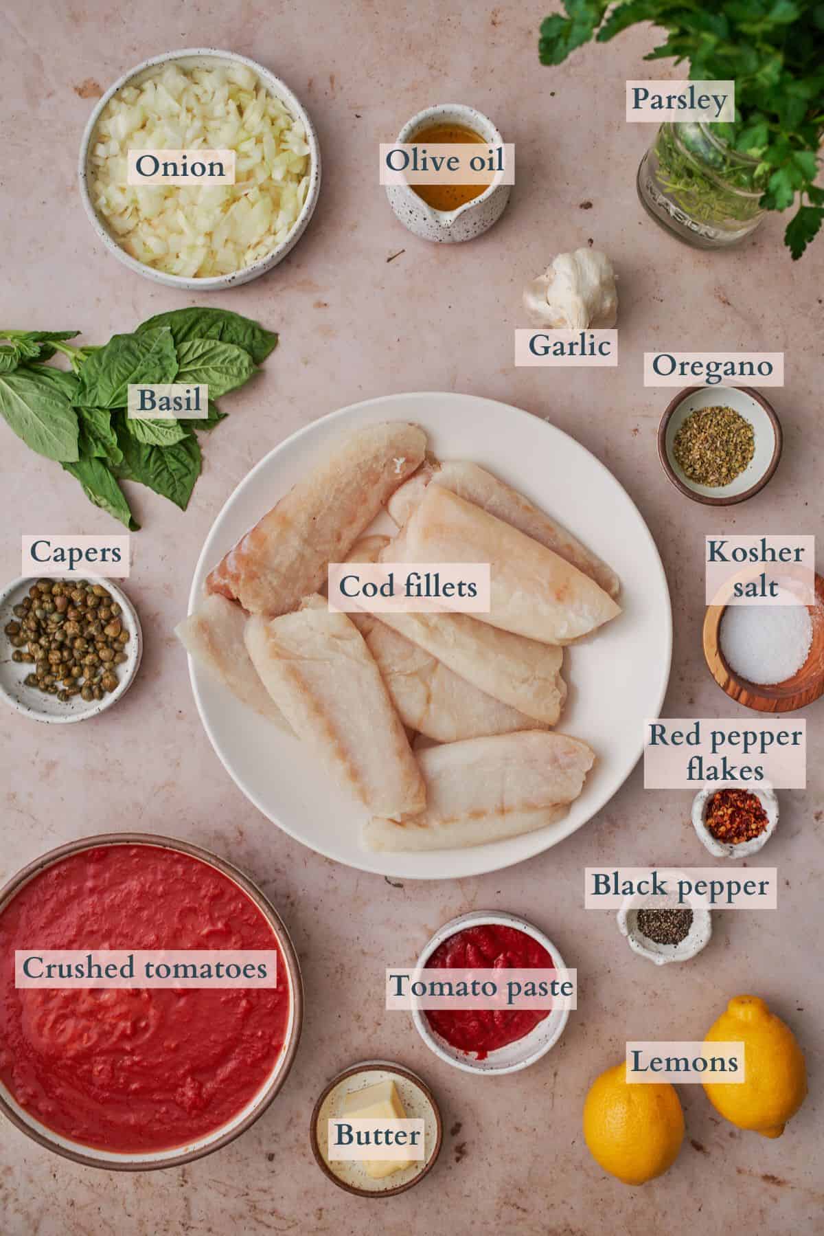 ingredients to make cod in tomato sauce, laid out in small bowls and on plates, labeled to denote each ingredient. 