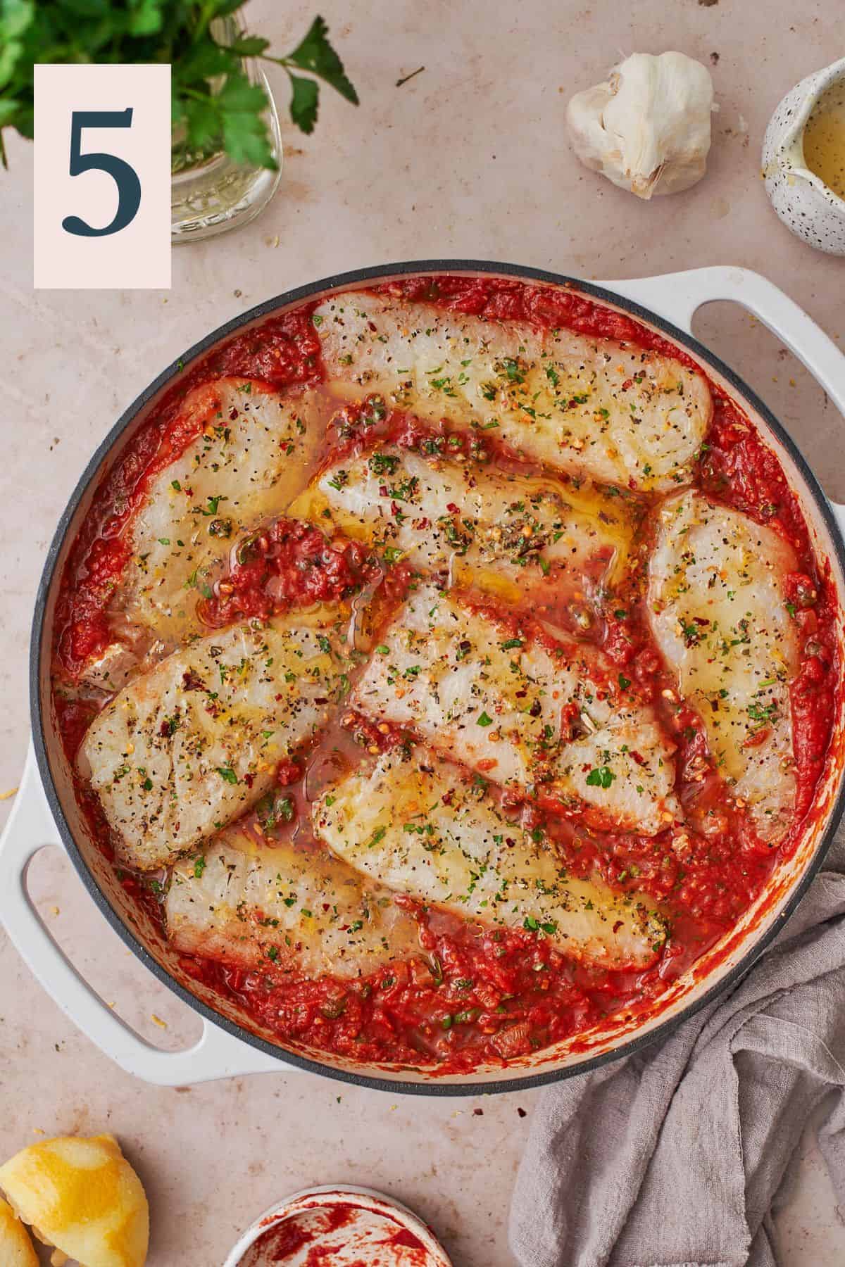 seasoned cod filets nestled into a tomato sauce in a skillet drizzled with olive oil.
