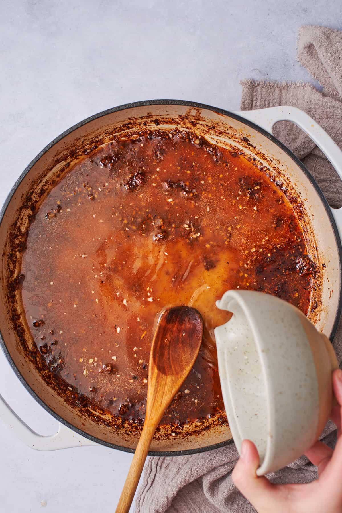 pouring chicken broth into a skillet with seasonings and garlic.