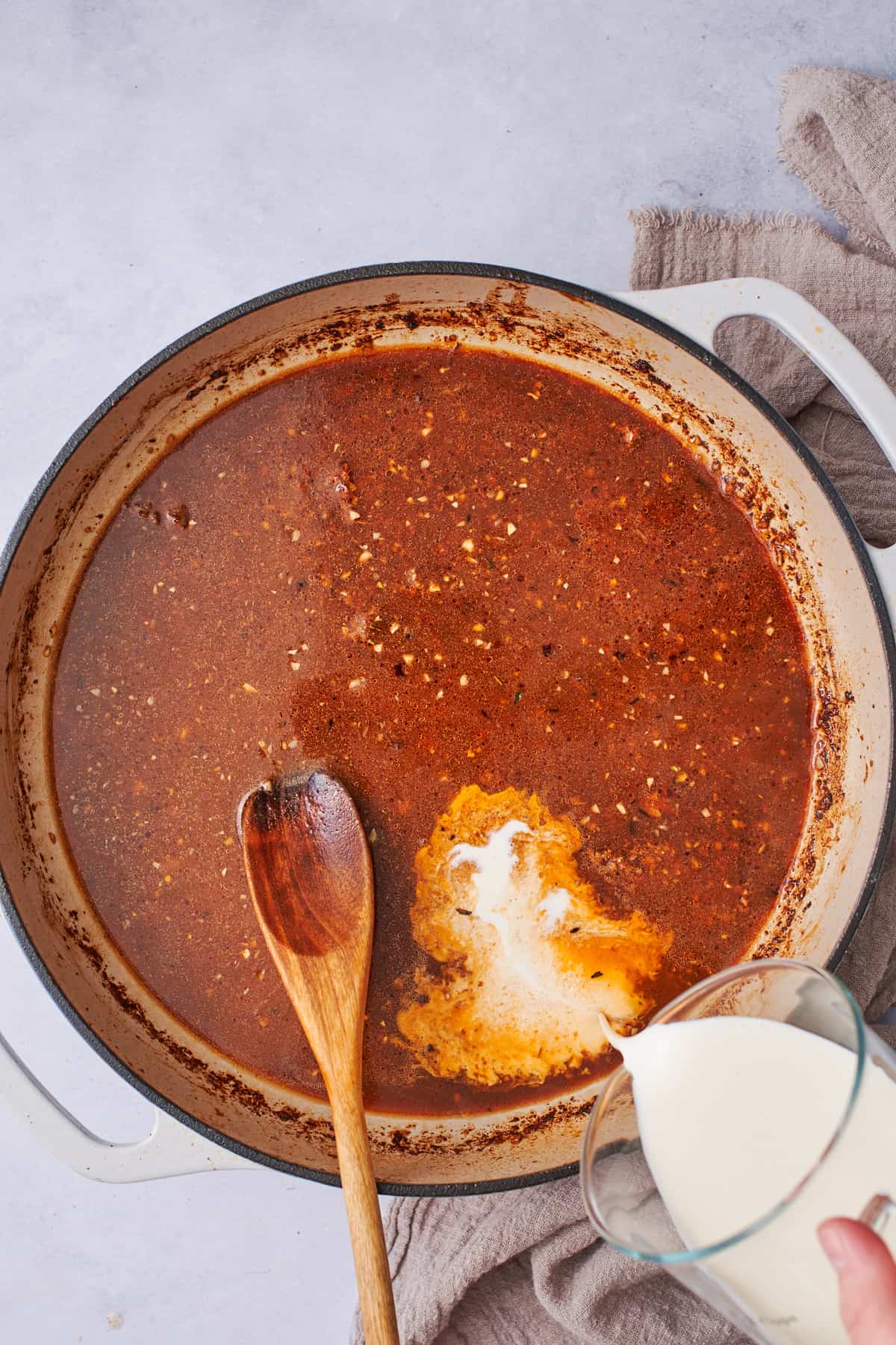 pouring cream into a spicy cajun broth in a skillet.