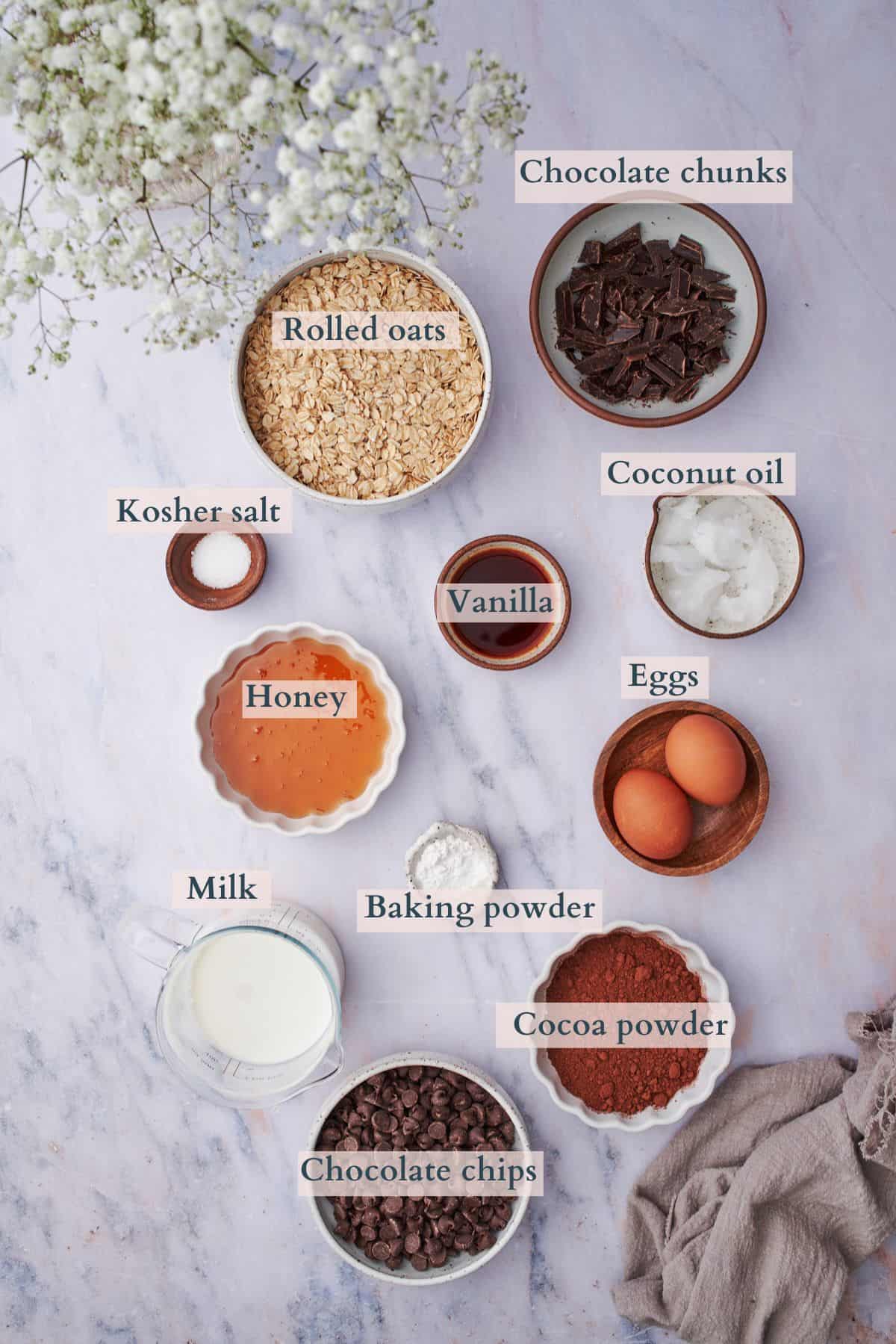ingredients to make chocolate baked oats laid out on a table with text to denote each ingredient. 