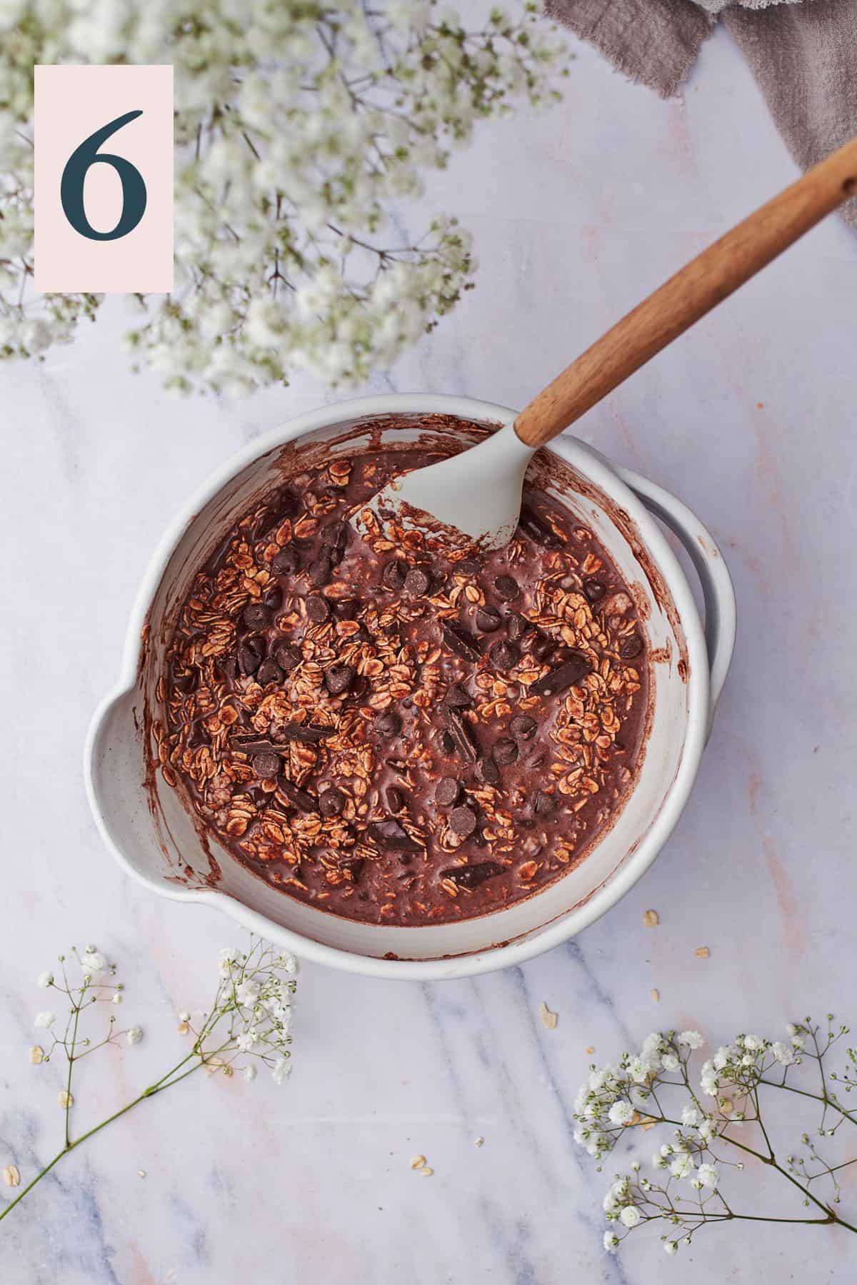 combined ingredients to make chocolate baked oats with chunks of chocolate in a mixing bowl with a rubber spatula.