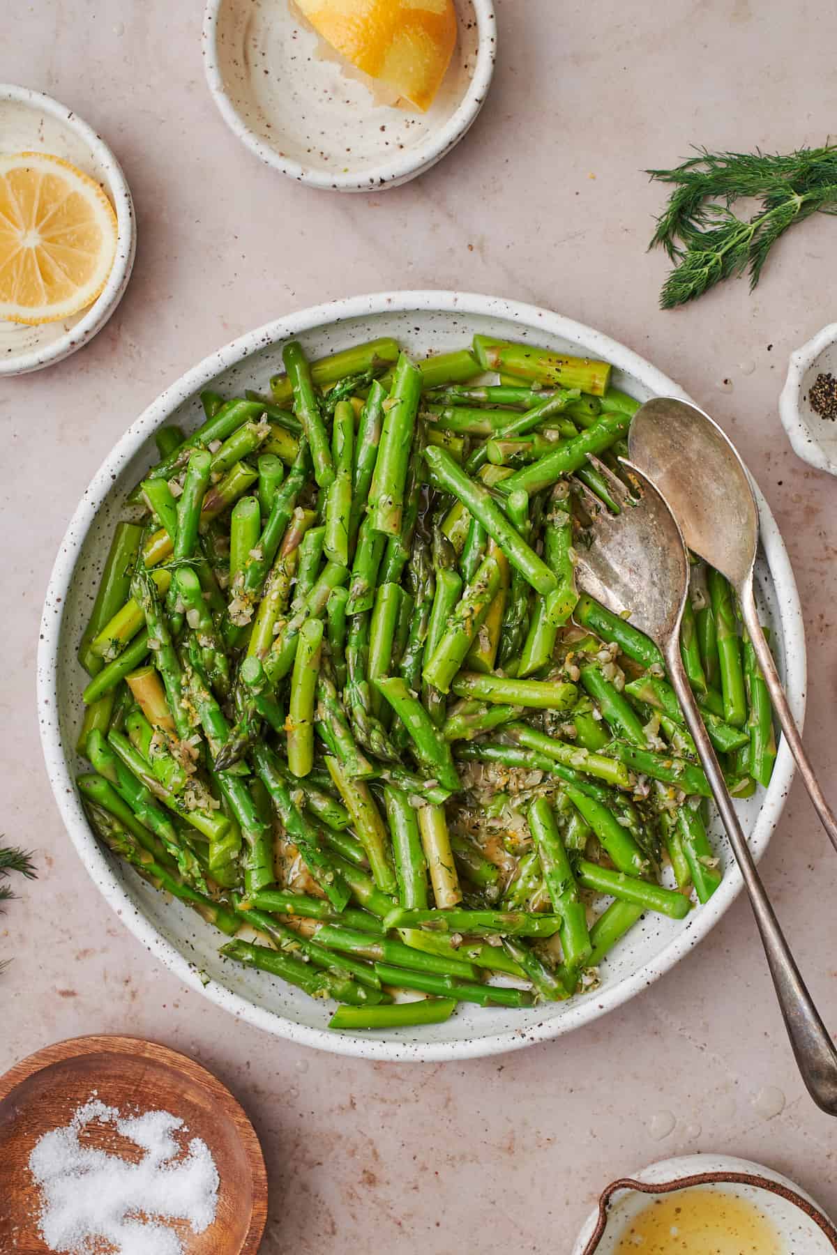 Blanched asparagus on a plate with silverware tossed with dressing.