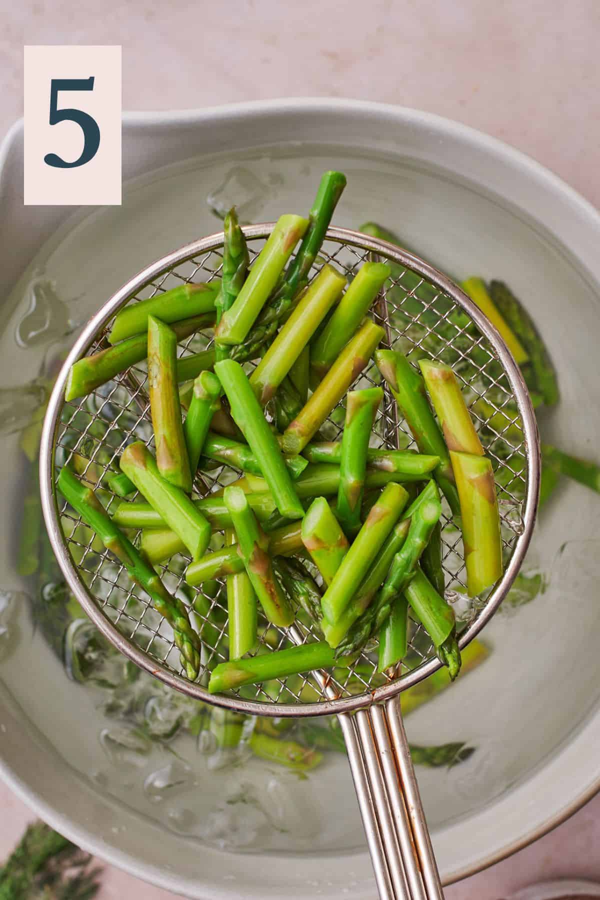 Removing asparagus from cold ice water with a strainer. 