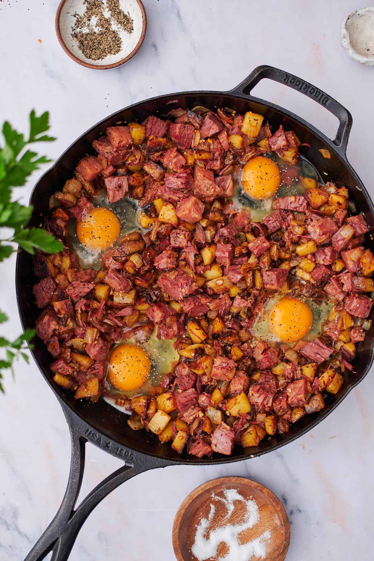 raw eggs in a skillet full of corned beef hash.