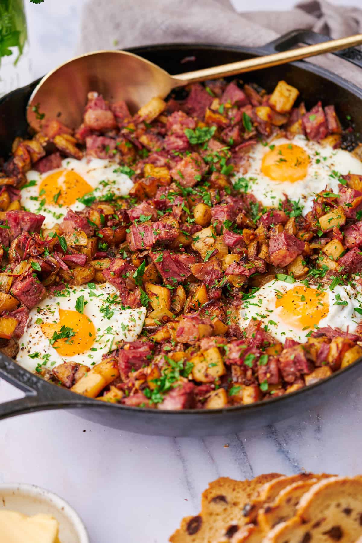 close up shot of corned beef hash in a cast iron skillet with eggs and parsley.