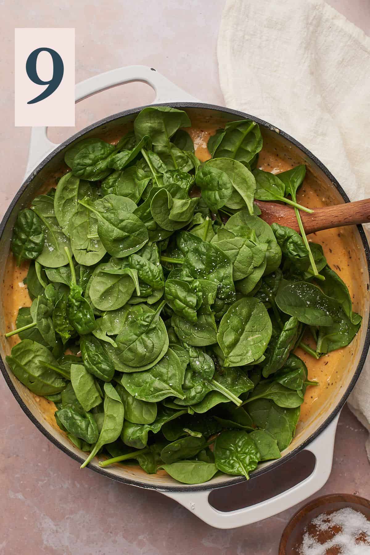 spinach added to a cream sauce in an enameled cast iron skillet. 