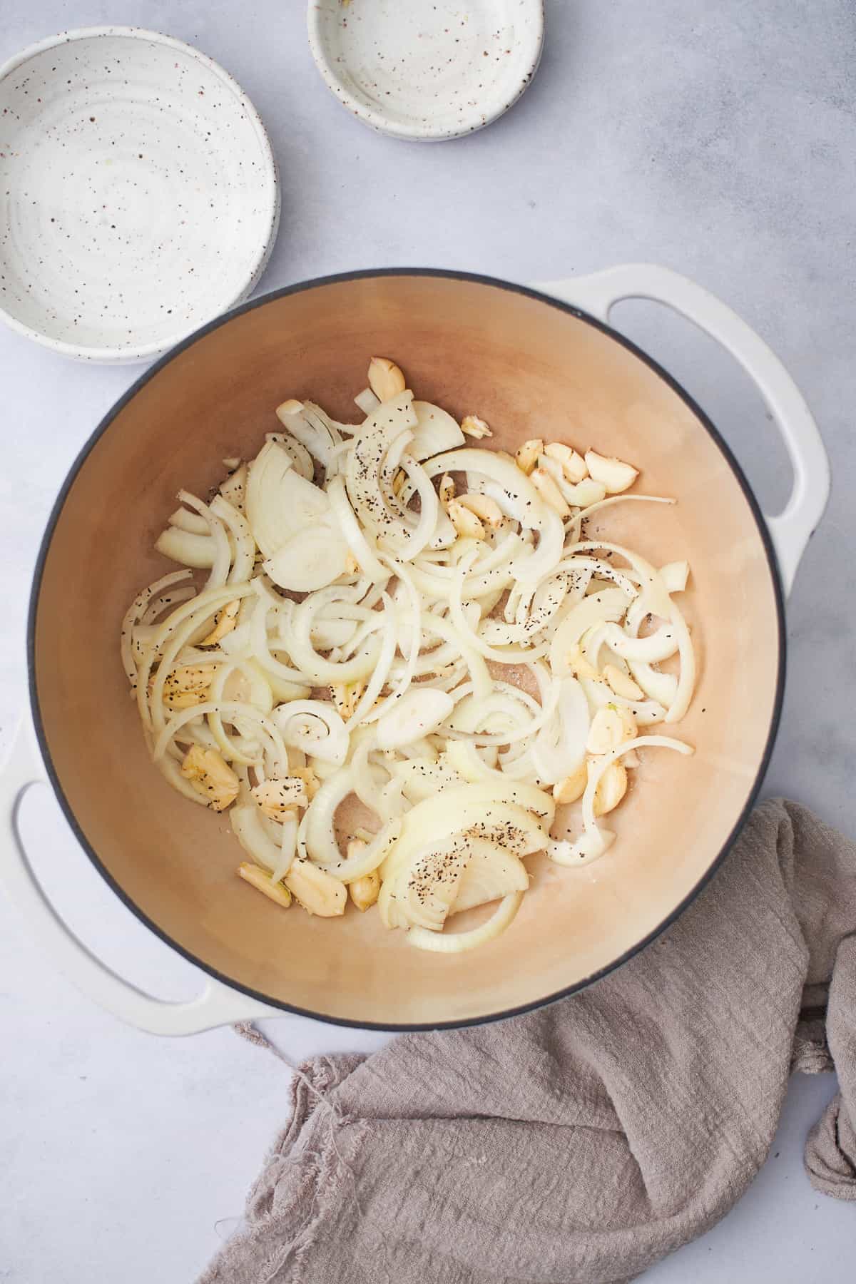 crushed garlic cloves and onions in a the bottom of the large white enameled Dutch oven with salt and pepper.