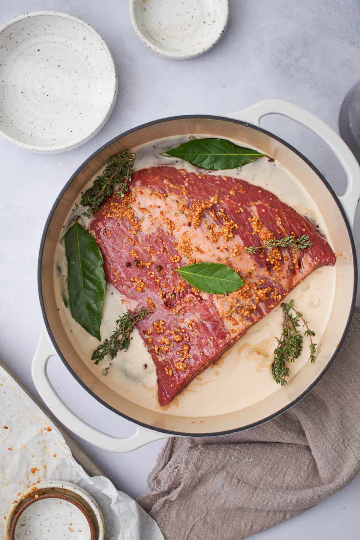 raw corned beef brisket in an enameled dutch oven with beef stock, creamy guinness beer, bay leaves, and fresh thyme.