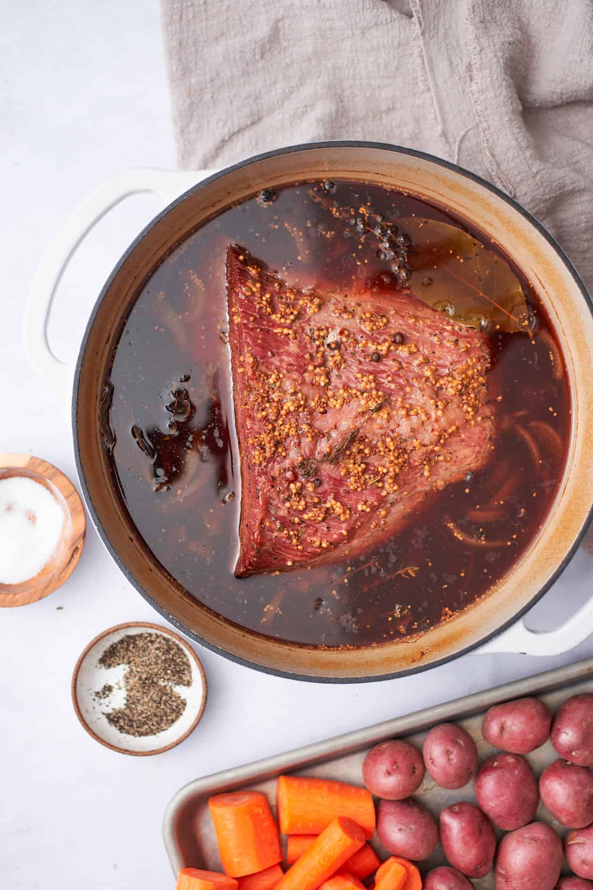 Partially cooked corned beef in a Dutch oven with broth, salt, and pepper.