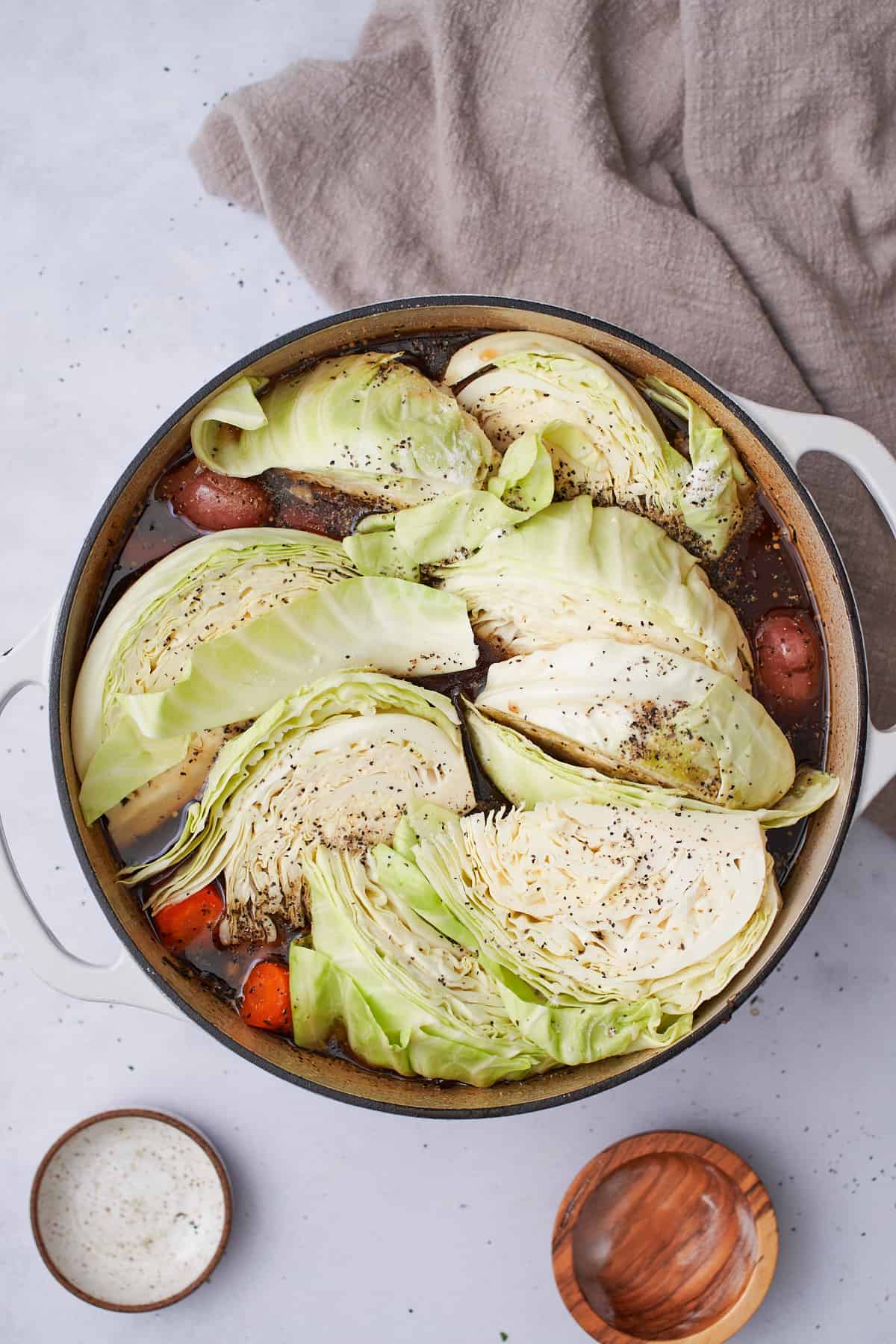 green cabbage wedges added to the top of a dutch oven seasoned with salt and pepper.