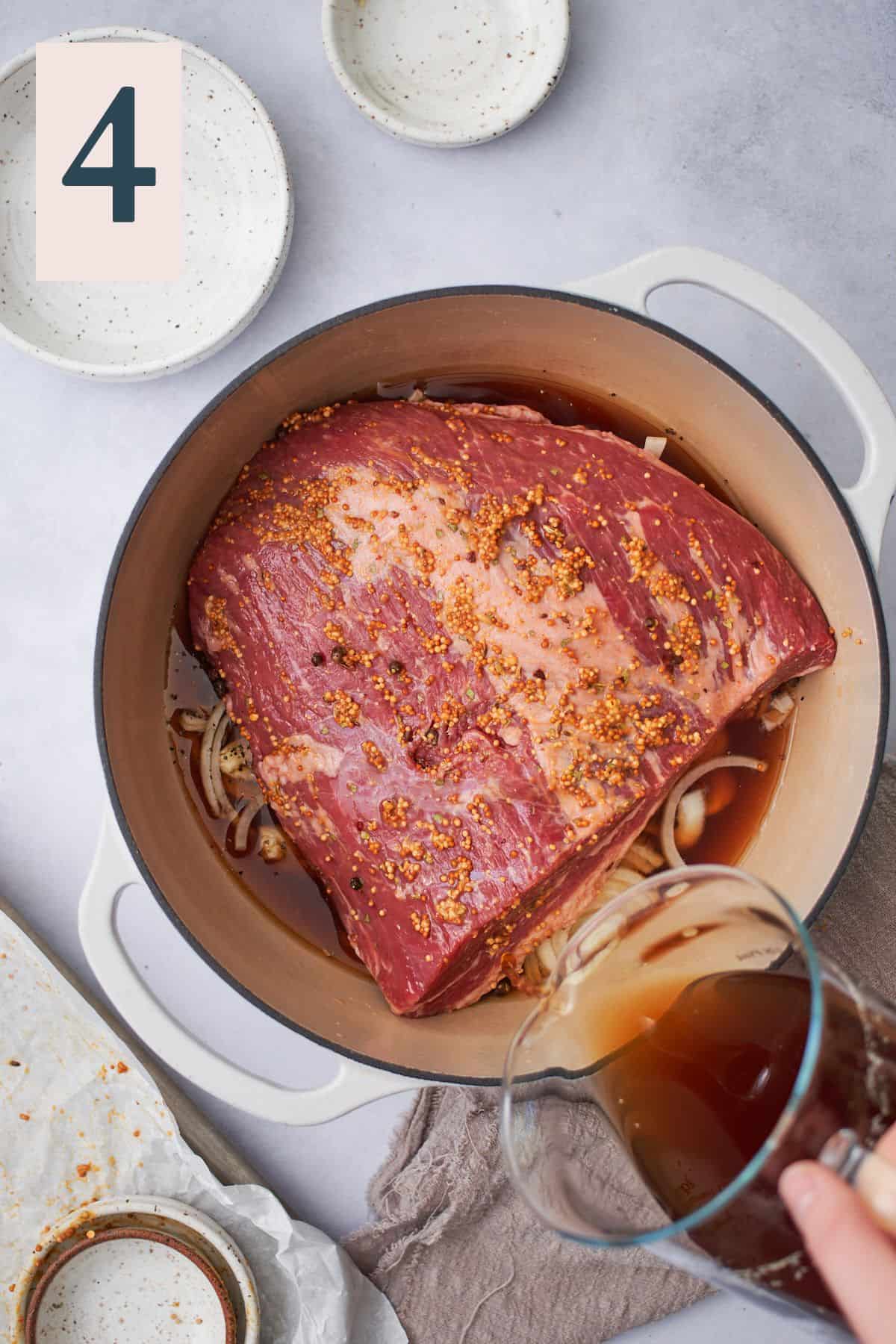pouring beef stock into an enameled dutch oven with seasoned corned beef inside. 