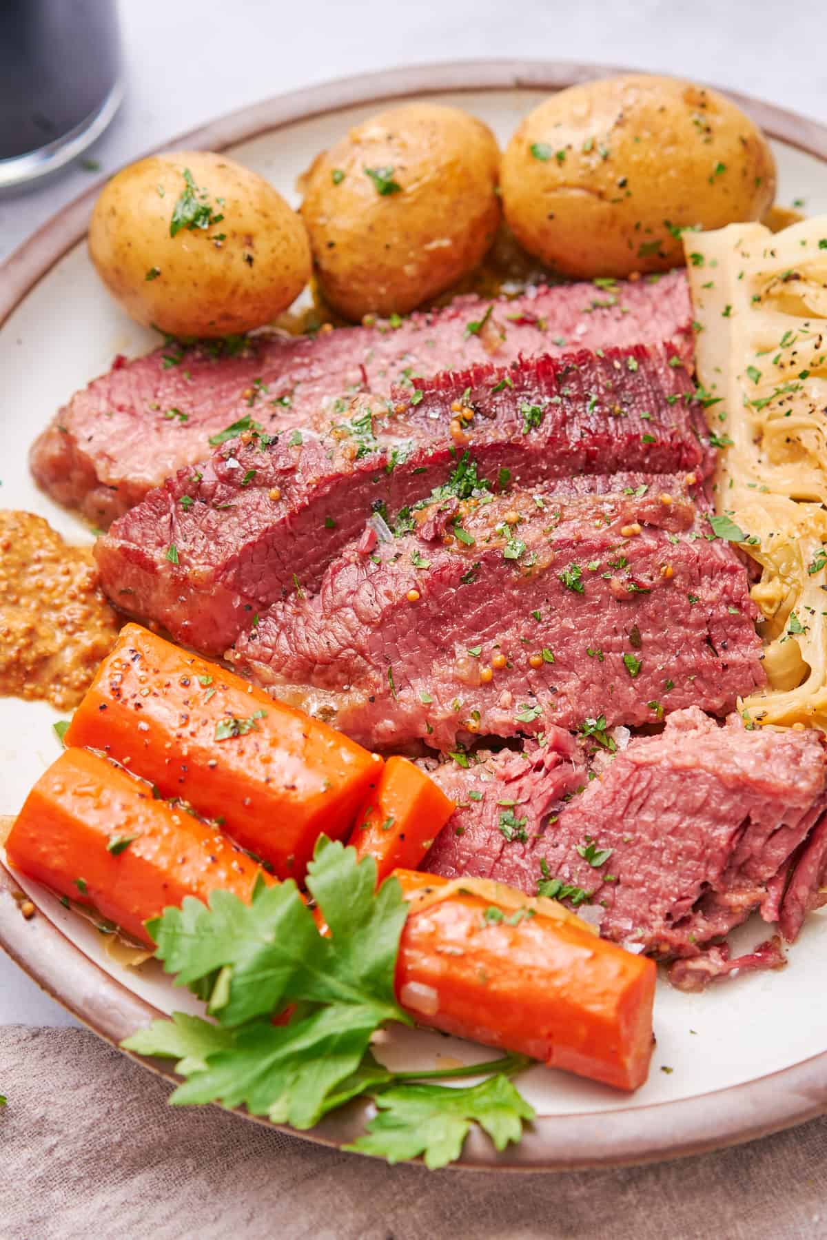 Corned beef slices on a plate with parsley, carrots, yellow potatoes, and cabbage. 