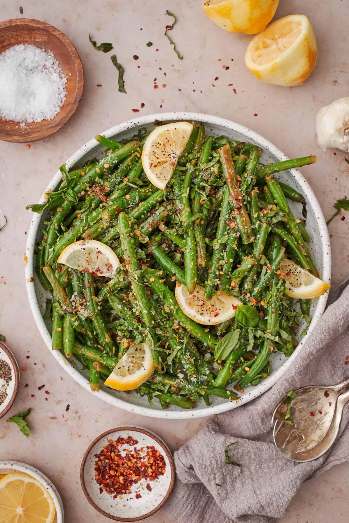 Lemon garlic green beans dish topped with lemon wedges, red pepper flakes, basil, and other ingredients.
