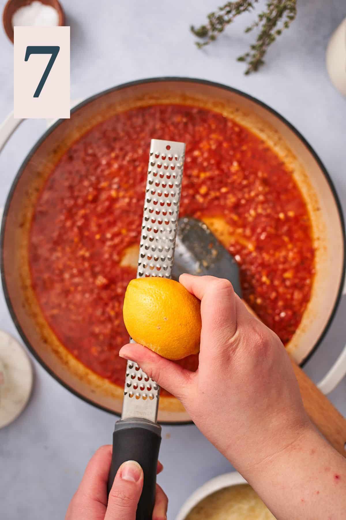 hand zesting lemon into a skillet with a tomato based sauce. 