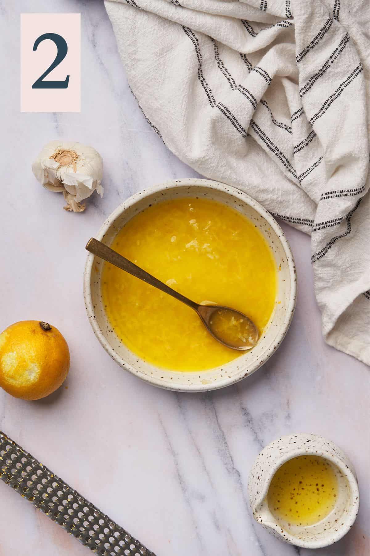 melted butter in a bowl surrounded by garlic, olive oil, and a zested lemon. 