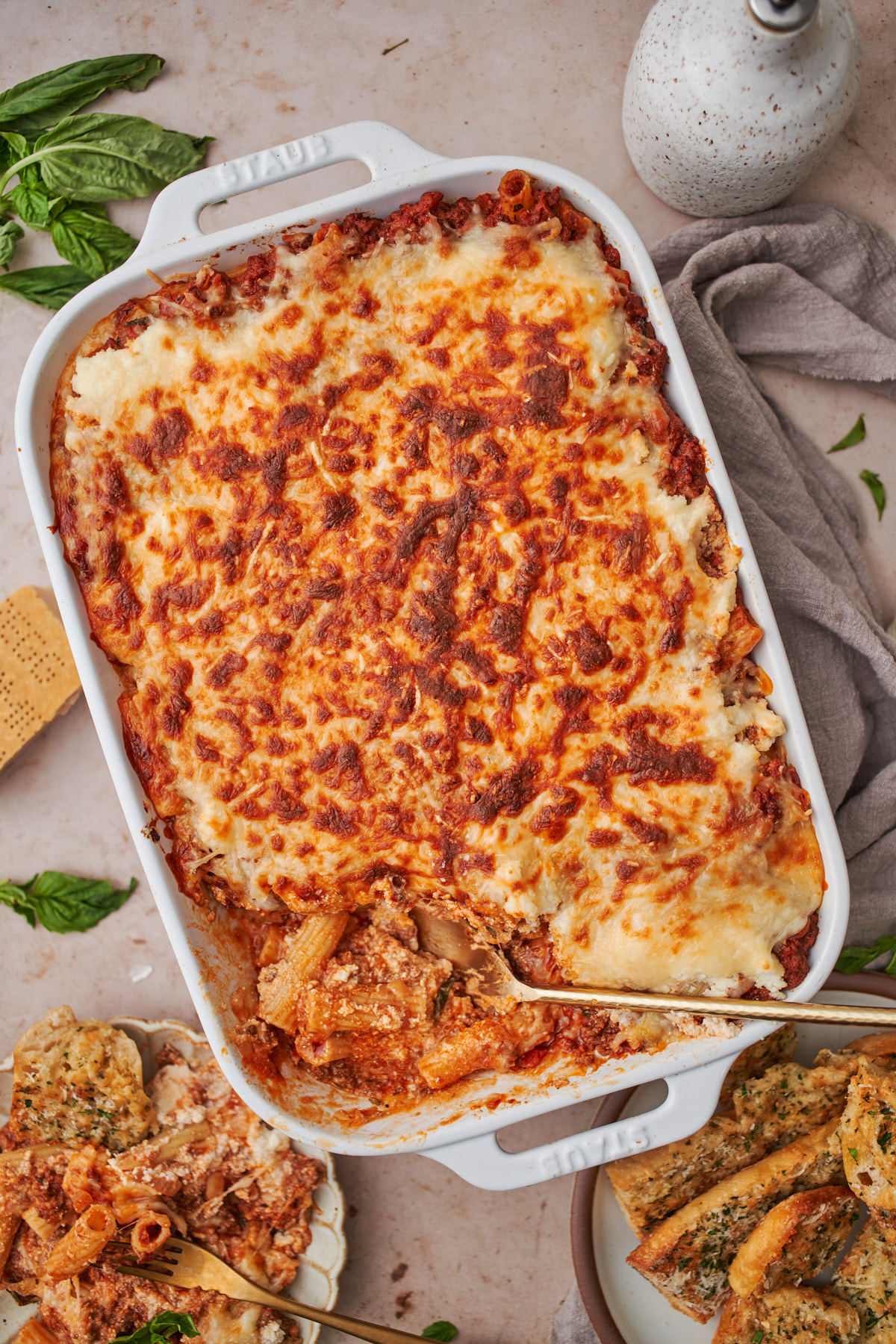 large casserole dish of baked rigatoni and garlic bread with a spoon full of cooked pasta. 