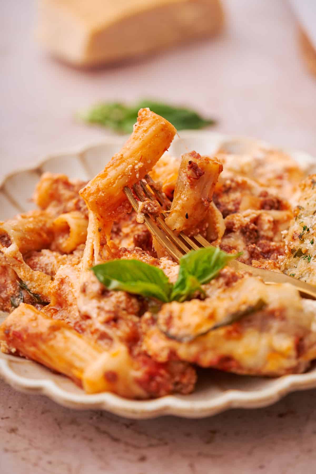 rigatoni on a plate with a fork stuck into the pasta, topped with basil. 