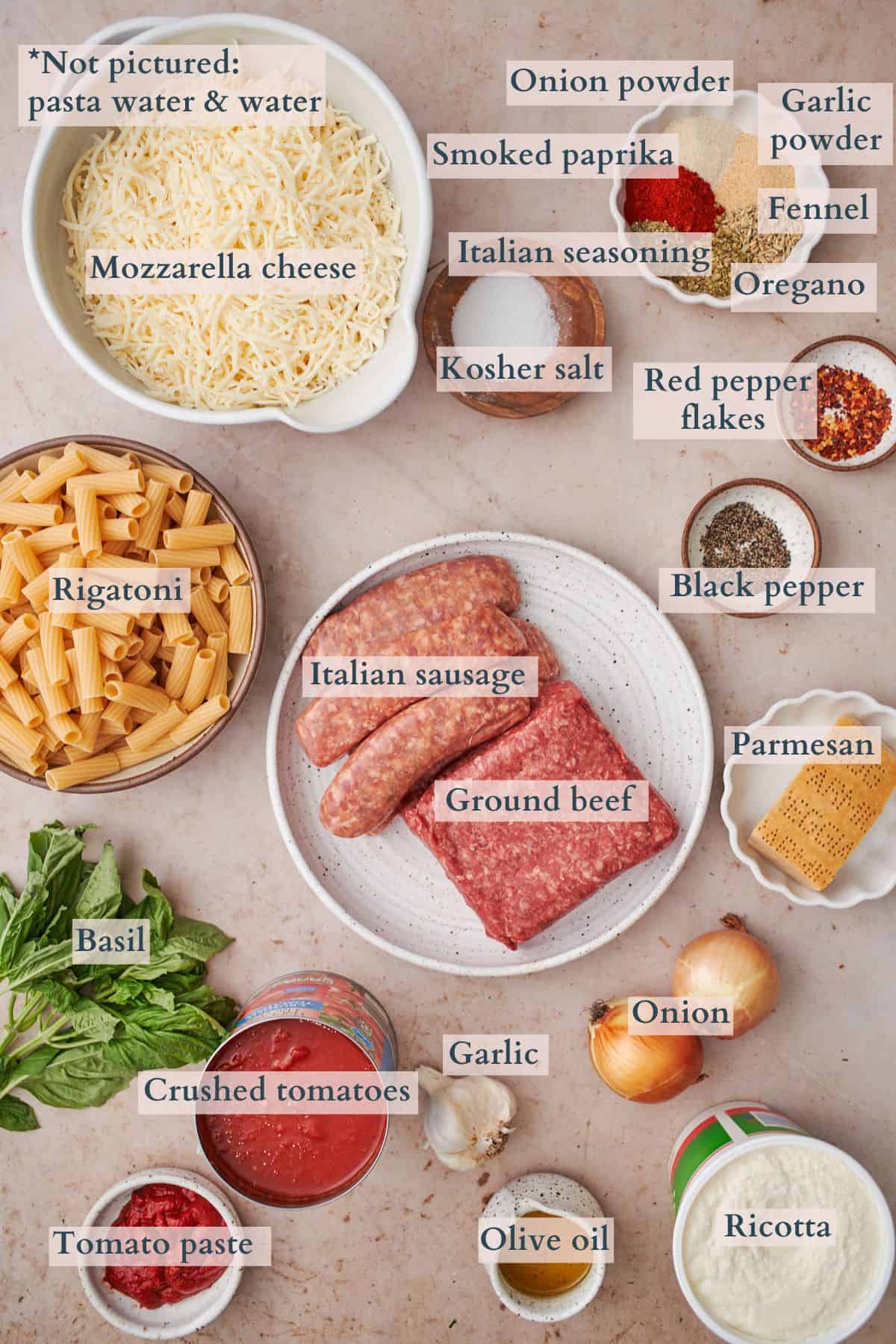 ingredients to make baked rigatoni with meat sauce laid out in bowls and on small plates labeled to denote each ingredient.