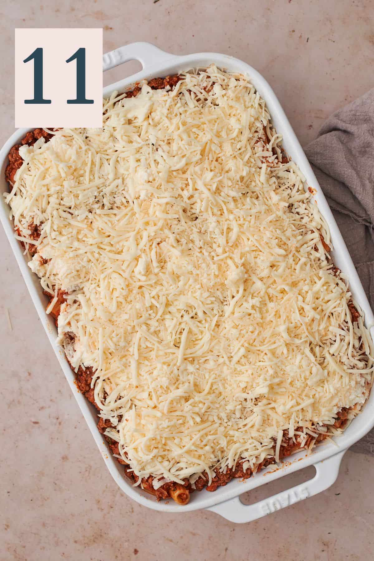 a layer of cheese over top of rigatoni in meat sauce in a rectangular baking dish.