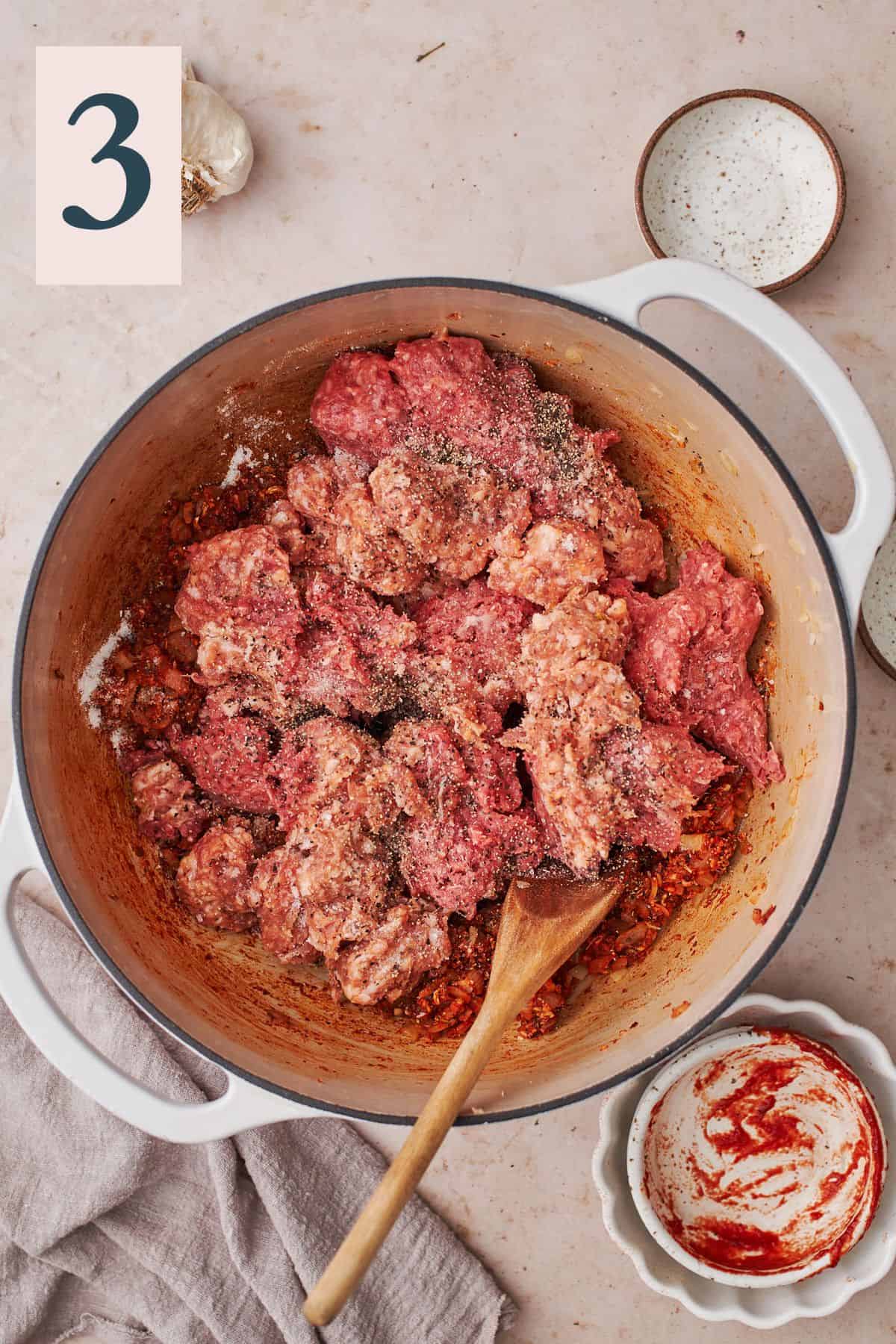 raw meat in a cast iron skillet with seasonings and cooked tomato paste, and onions. 